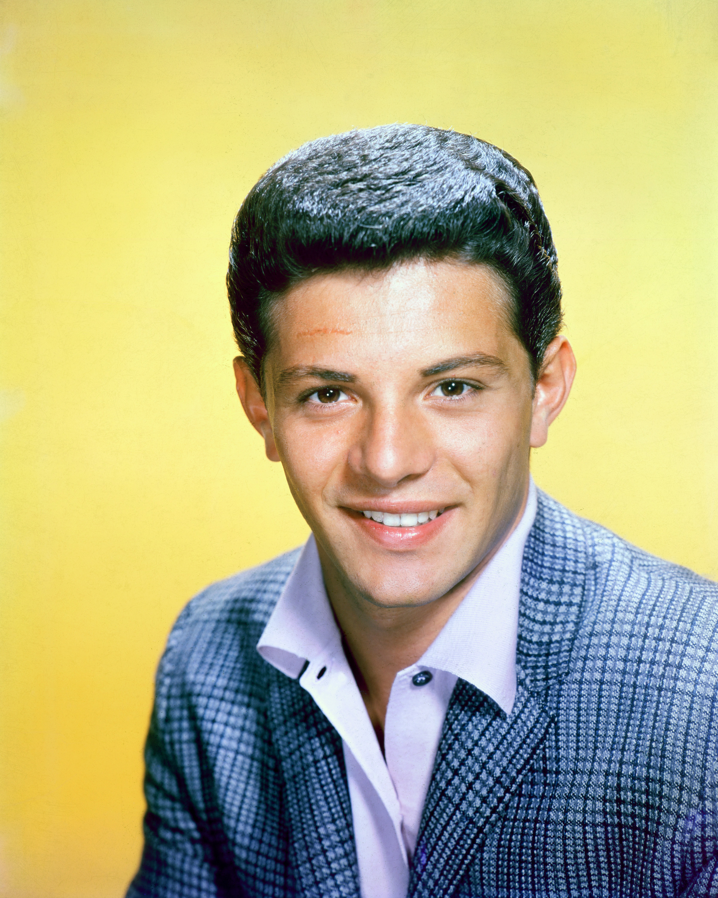 Frankie Avalon, US singer and actor, wearing a blue tweed jacket in a studio portrait, against a yellow background, circa 1960. | Source: Getty Images