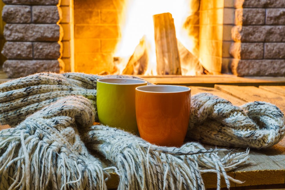 A photo of two mugs and wool scarves near cozy fireplace. | Photo: Shutterstock