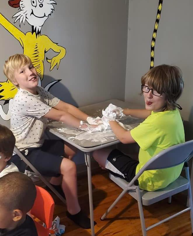 Caleb Moore is in a white shirt with polka dots as he photographs with a boy who sticks his tongue out while dressed in a lemon shirt, from a post dated June 12, 2025 | Source: Facebook/AshleyBentz