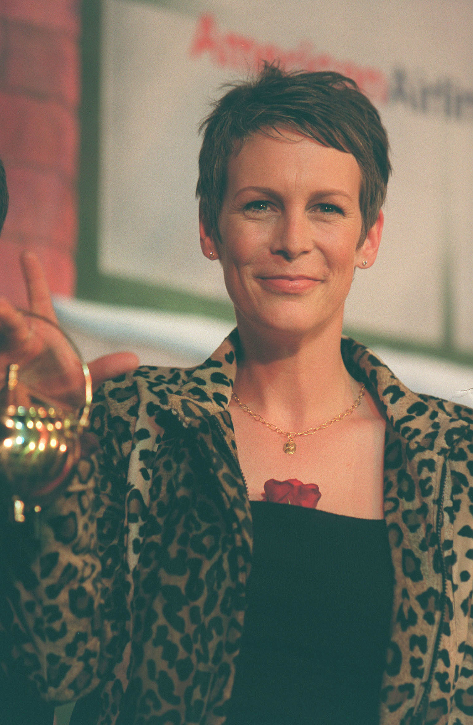 Jamie Lee Curtis embraces bold style in a leopard-print jacket and short pixie cut, flashing a warm smile during a portrait session around 2000.