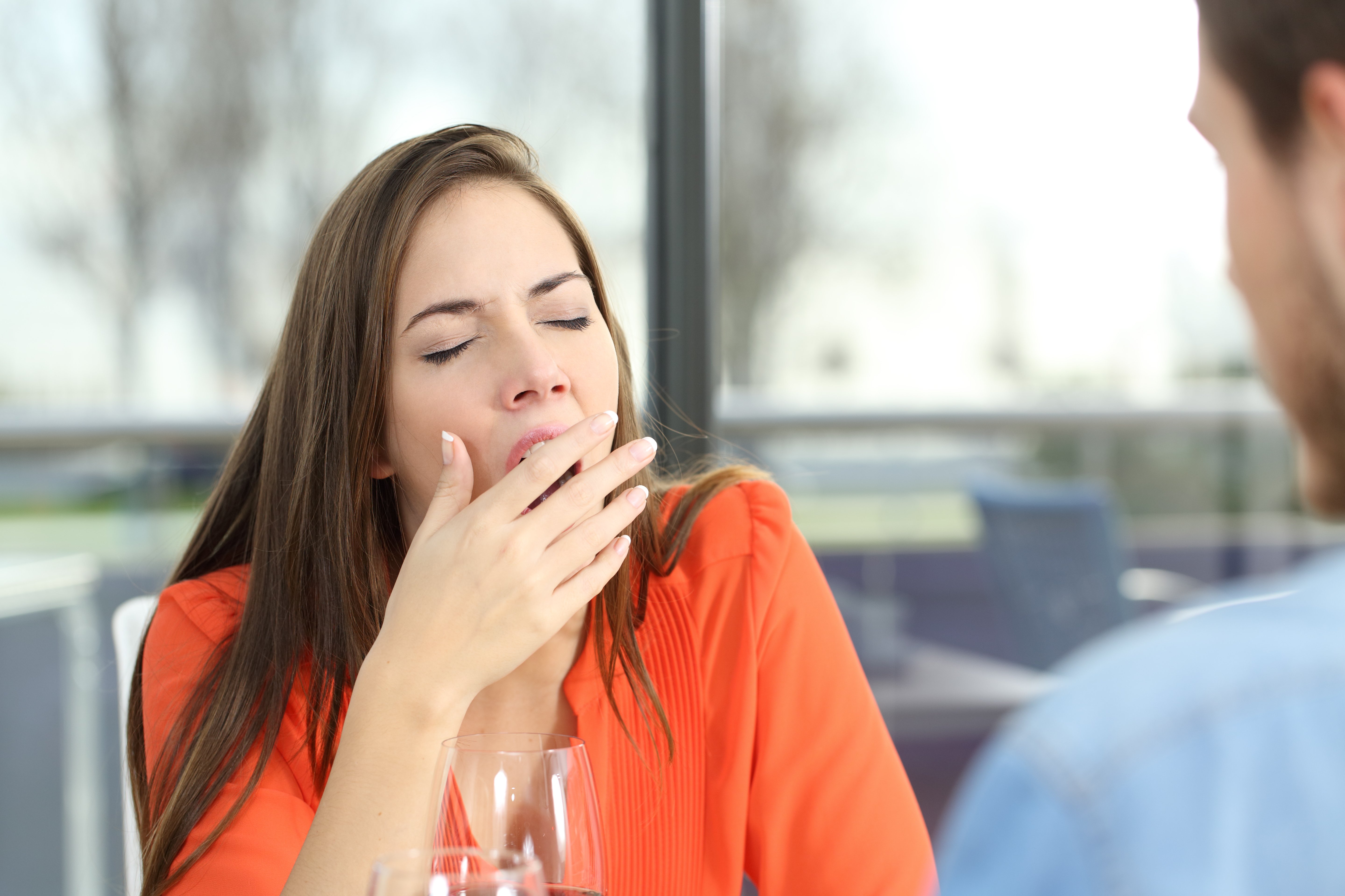 Photo of woman yawning while sitting at a table with a man. | Source: Shutterstock