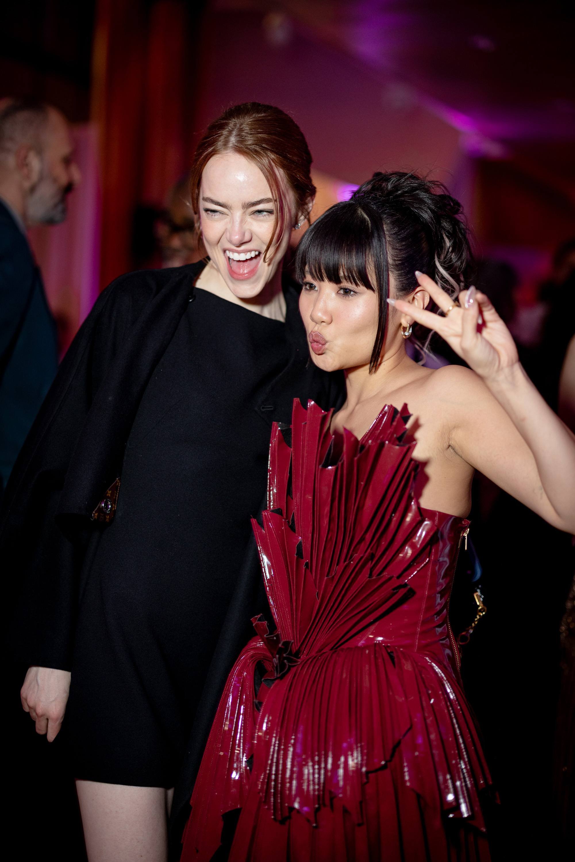 Emma Stone poses playfully alongside Rei Ami, laughing wide as the singer flashes a peace sign, capturing a lively moment from the evening celebration.