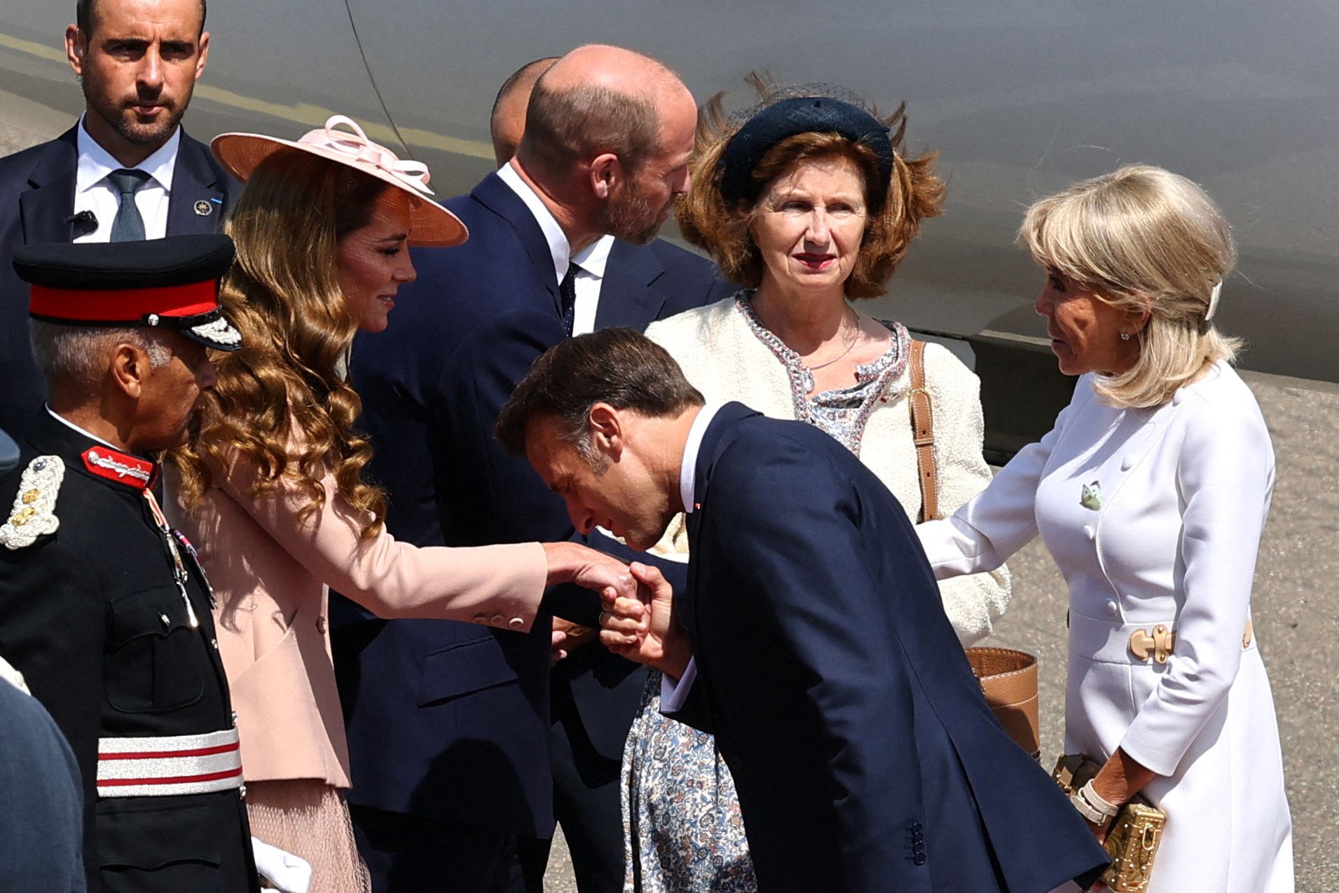 French President Emmanuel Macron bows and kisses Princess Catherine's hand upon arriving at RAF Northolt while Mrs. Brigitte Macron stands behind him.