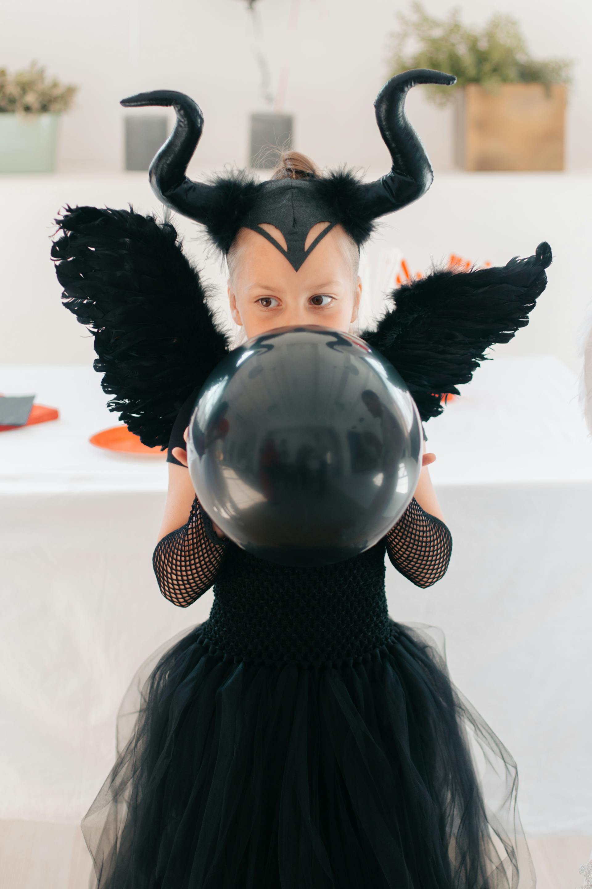 Een jong meisje in een zwart Halloweenkostuum met een ballon in haar hand | Bron: Pexels