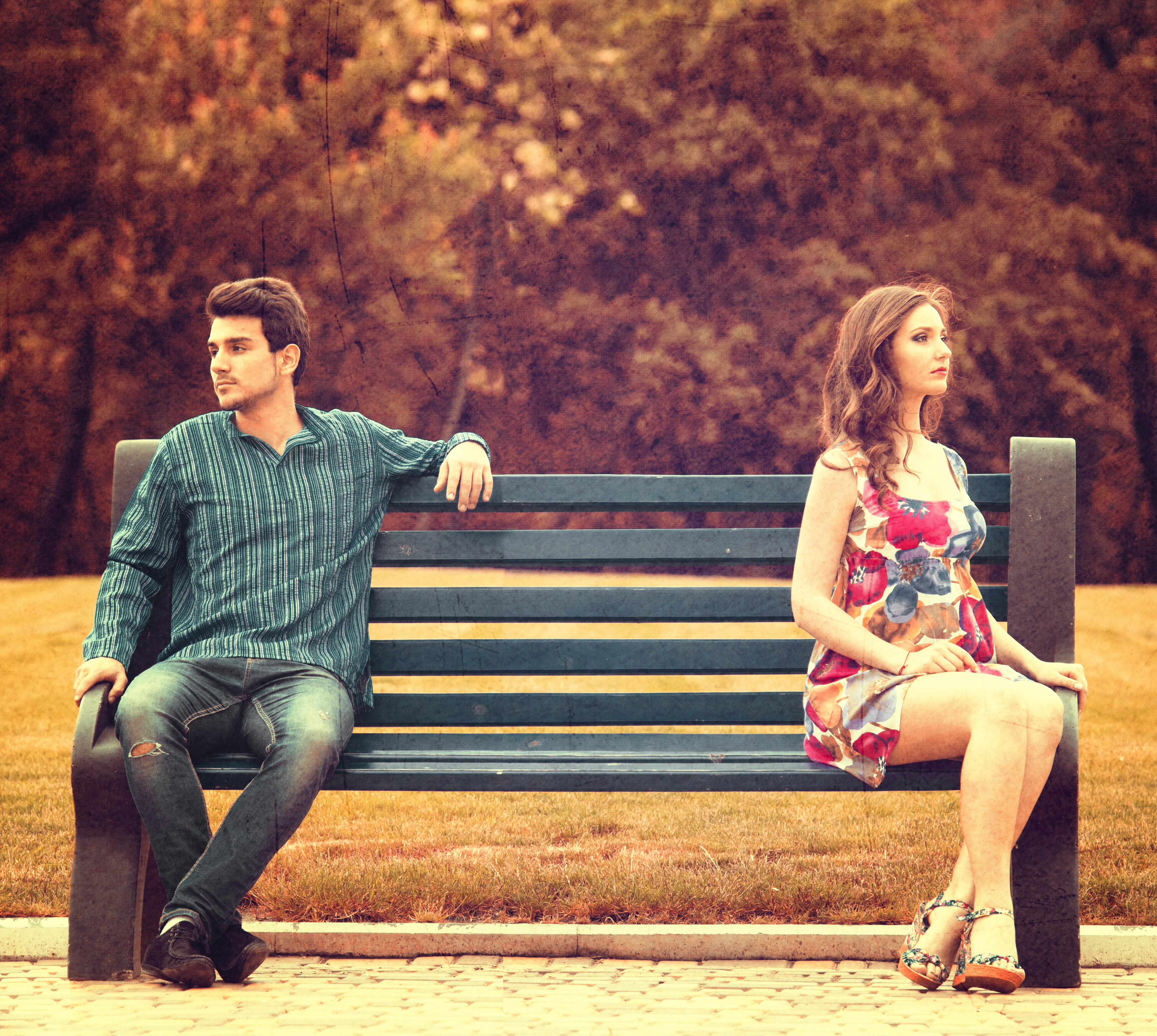 A young couple sitting apart on a park bench | Source: Shutterstock