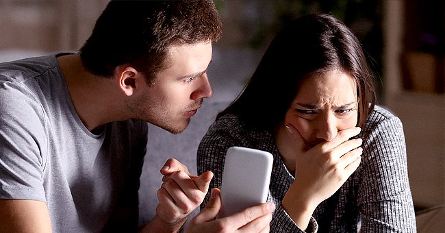 A man points at a cellphone while shouting at a woman who looks very upset. | Photo: Shutterstock