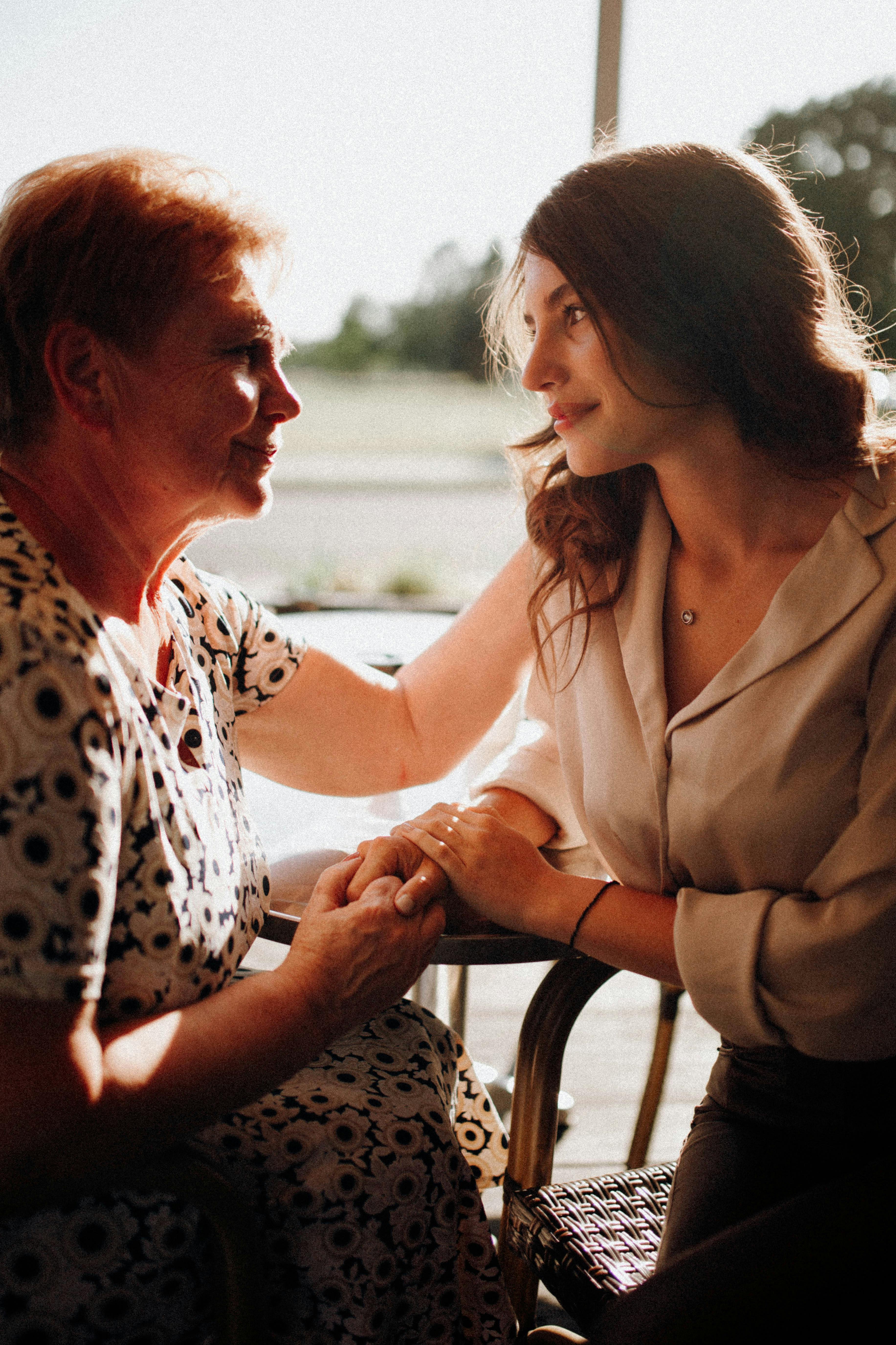 Madre e hija sentadas a la mesa cogidas de la mano | Fuente: Pexels