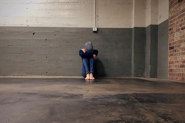 Girl sits against wall with head between knees | Photo: Pixabay