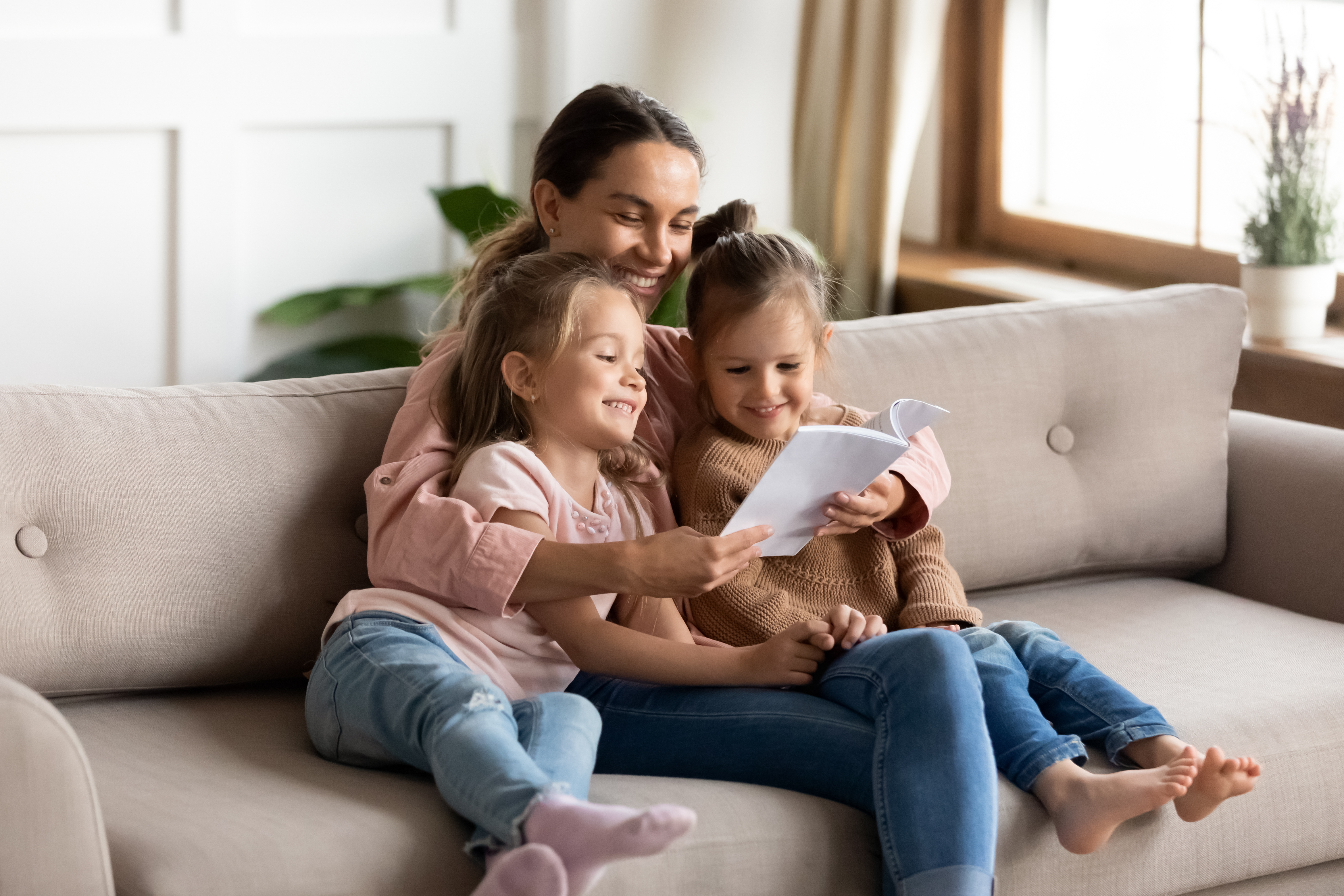 A young mother reads a book to her little daughters while sitting on the sofa at home | Source: Shutterstock