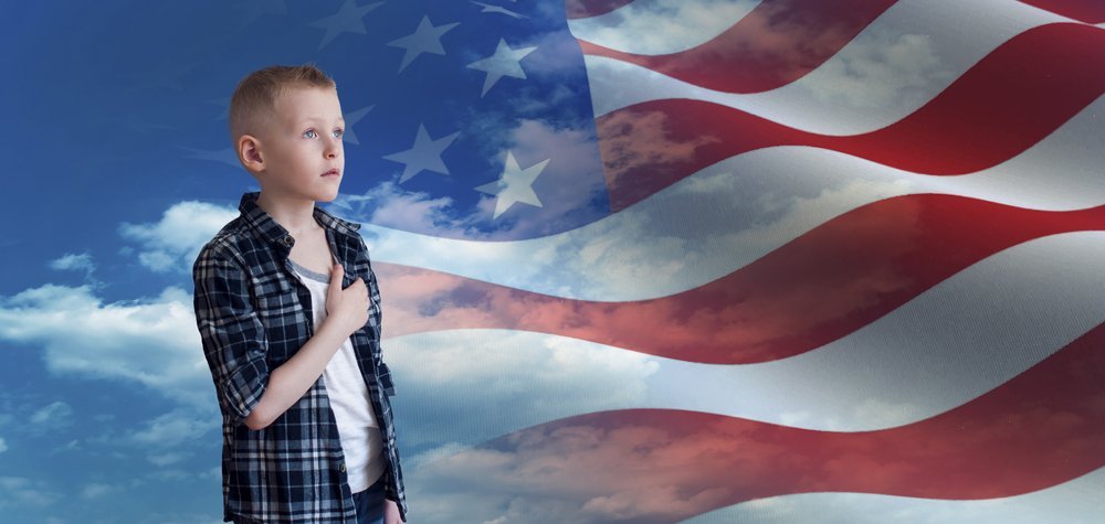 Junge mit Hand auf dem Herzen vor der Amerikanischen Flagge | Quelle: Shutterstock