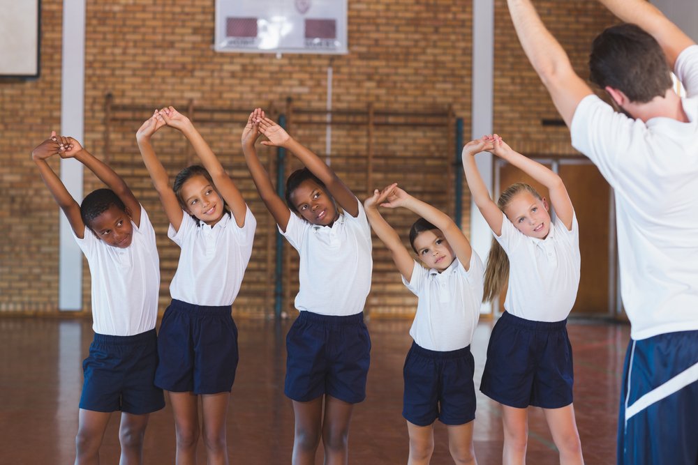Profesor enseñando ejercicio a niños de escuela en la cancha de baloncesto en el gimnasio de la escuela. I Foto: Shutterstock