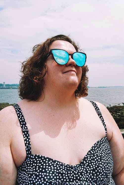 Mujer posando en la playa mientras usa un traje de baño de talla grande con estampado de lunares y gafas de sol. | Foto: Pexels