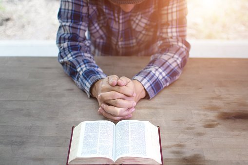  Hands folded in prayer on a Holy Bible in church concept for faith, spirituality and religion | Photo: Getty Images