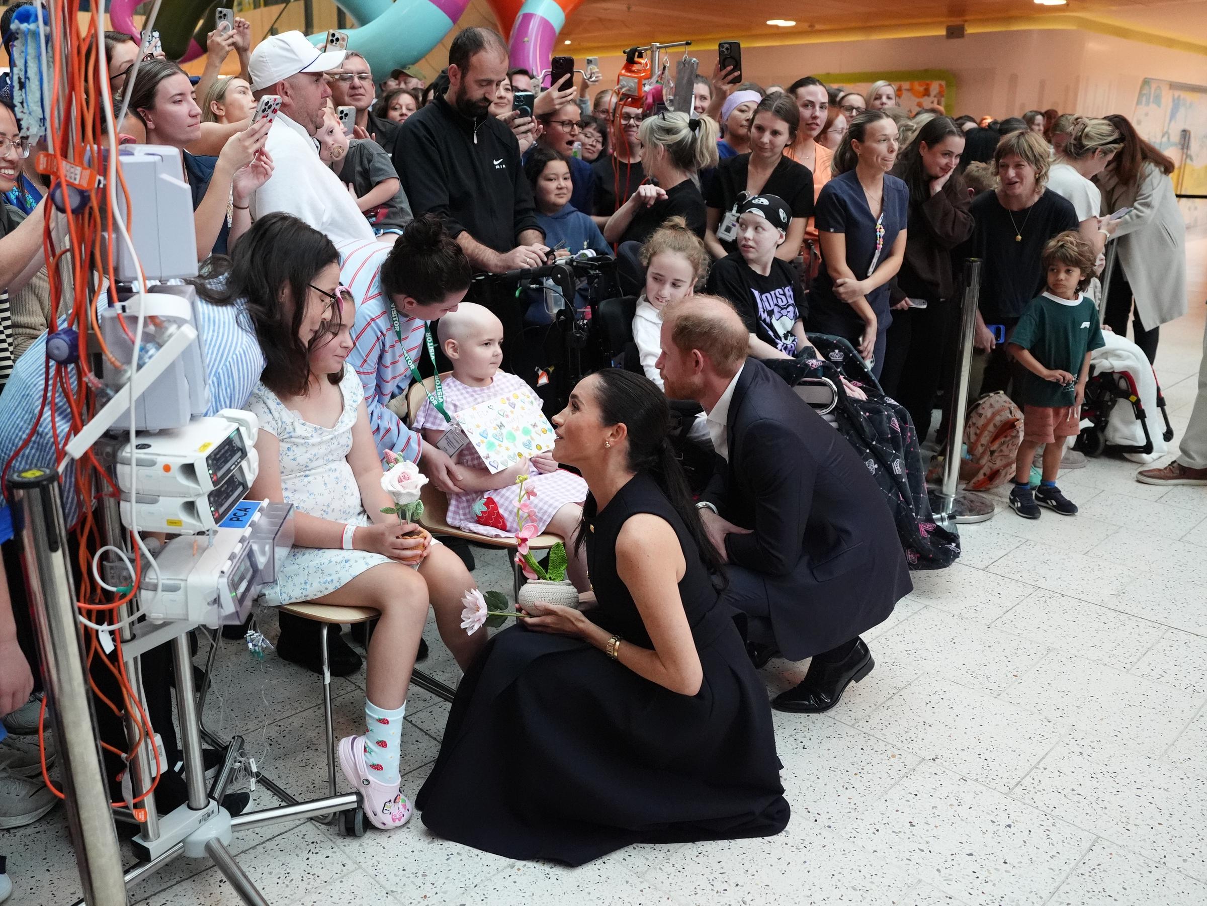 Meghan, Duchess of Sussex, and Prince Harry, Duke of Sussex, kneel beside young patients as they share a warm exchange during their visit to the Royal Children's Hospital in Melbourne on 14 April 2026. | Source: Getty Images