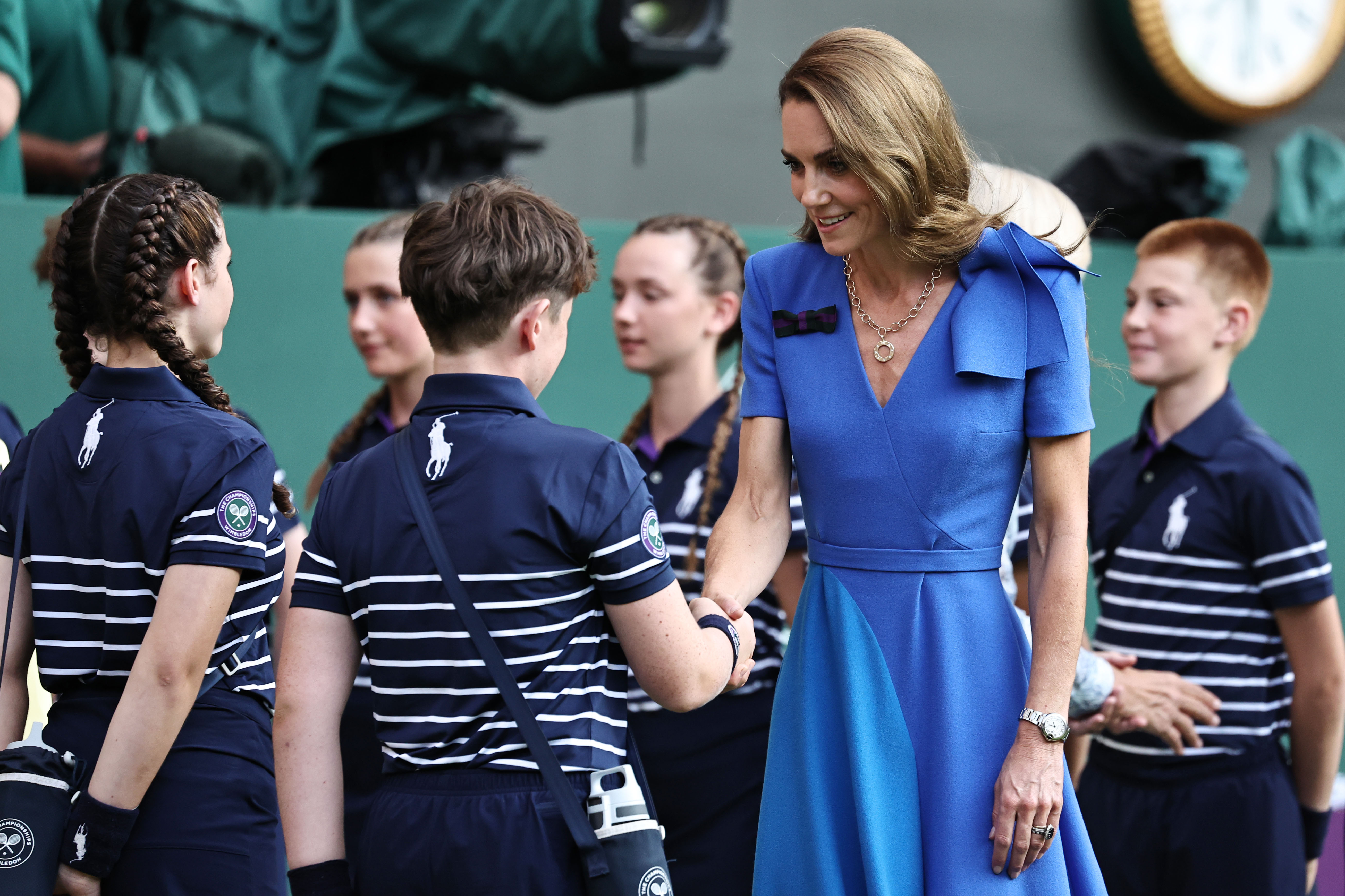 Princess Catherine greets the Wimbledon ball boys and girls with a smile during the award ceremony. She bends slightly as she extends a hand, engaging warmly with the young team.