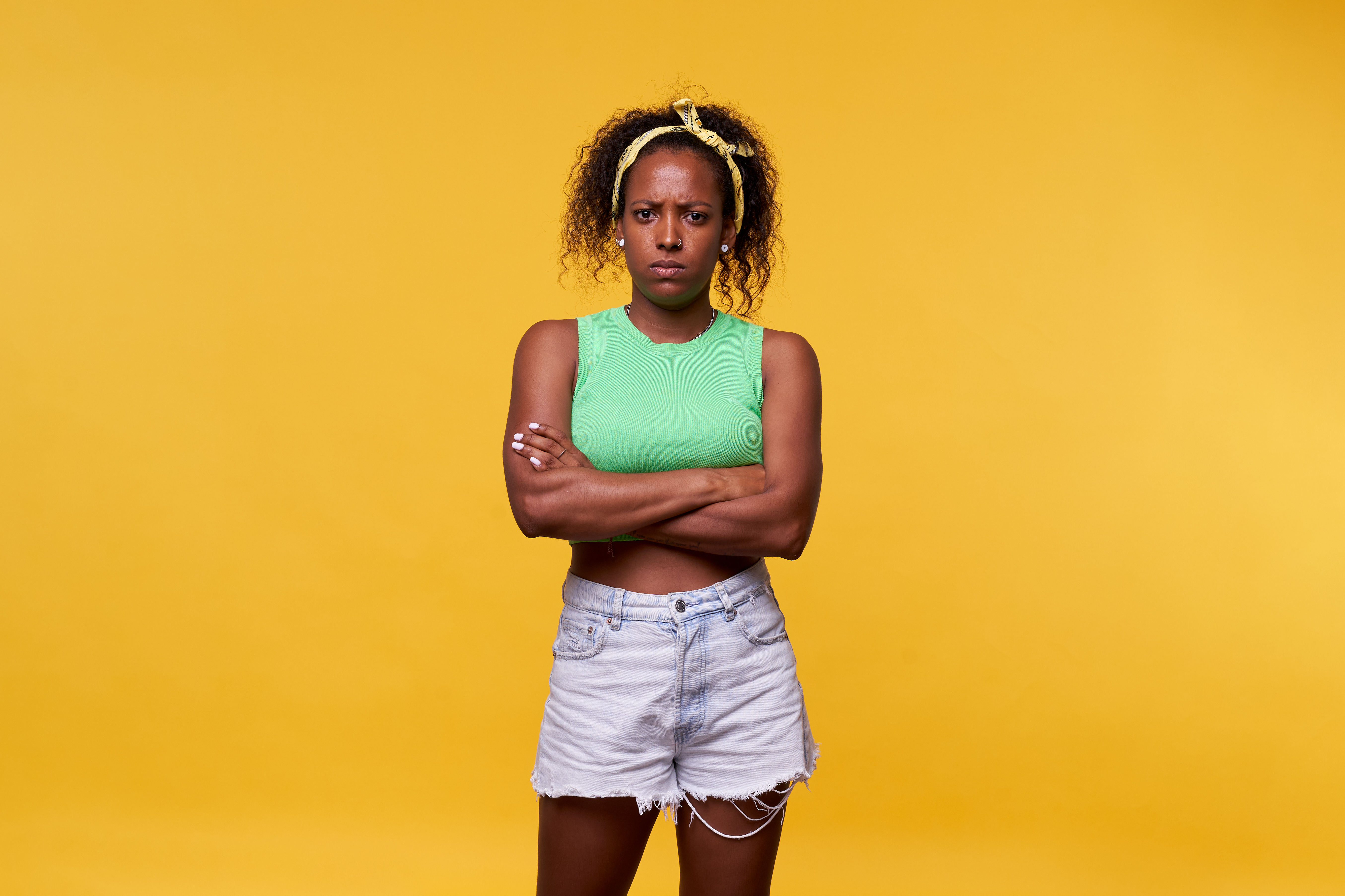 Photo of an angry Latin woman standing against a yellow background crossing arms and looking at camera seriously. Isolated image at studio | Source: Getty Images