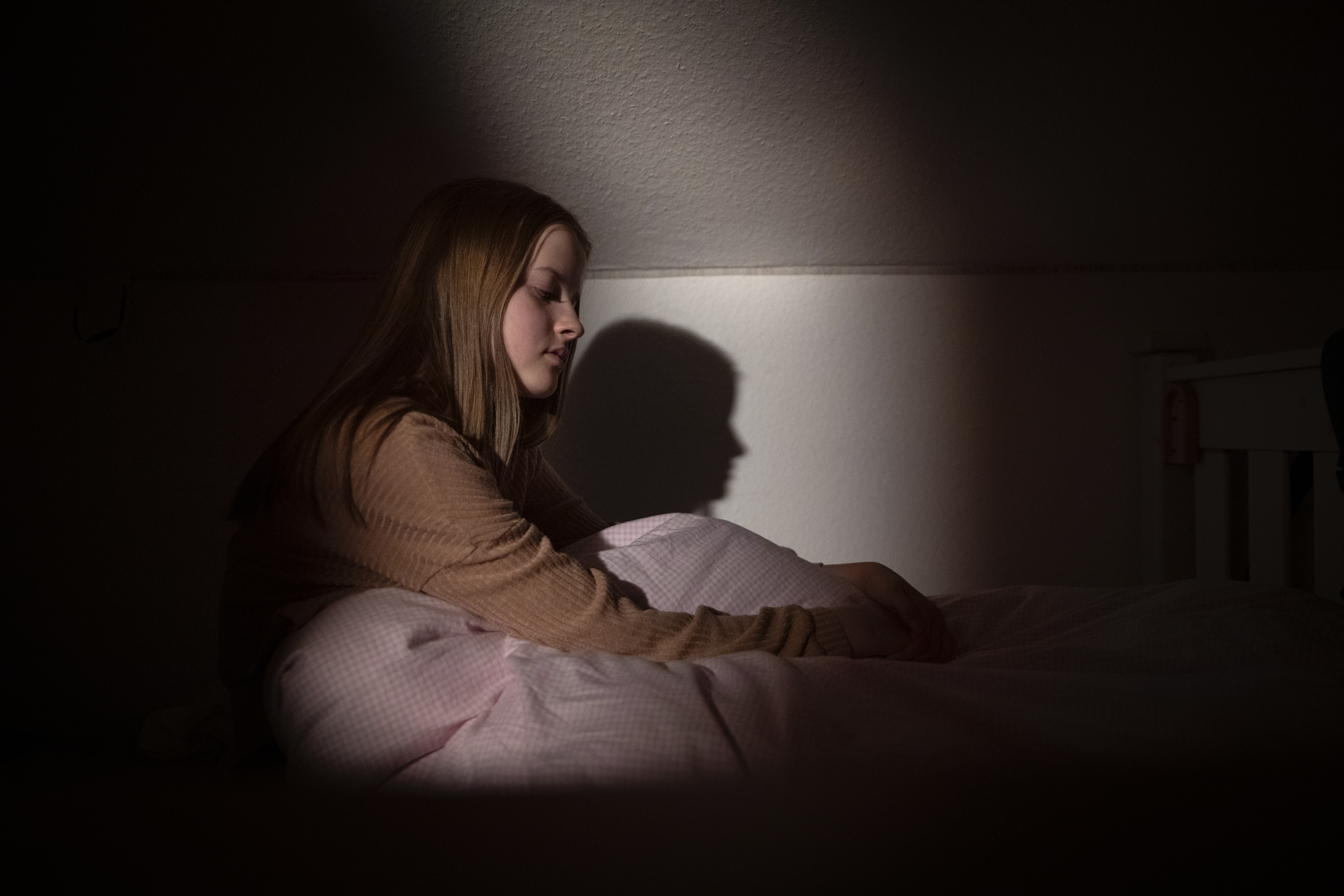 Teenage girl sitting up in bed at nighttime in low light with facial expression depicting despair and sadness | Source: Getty Images