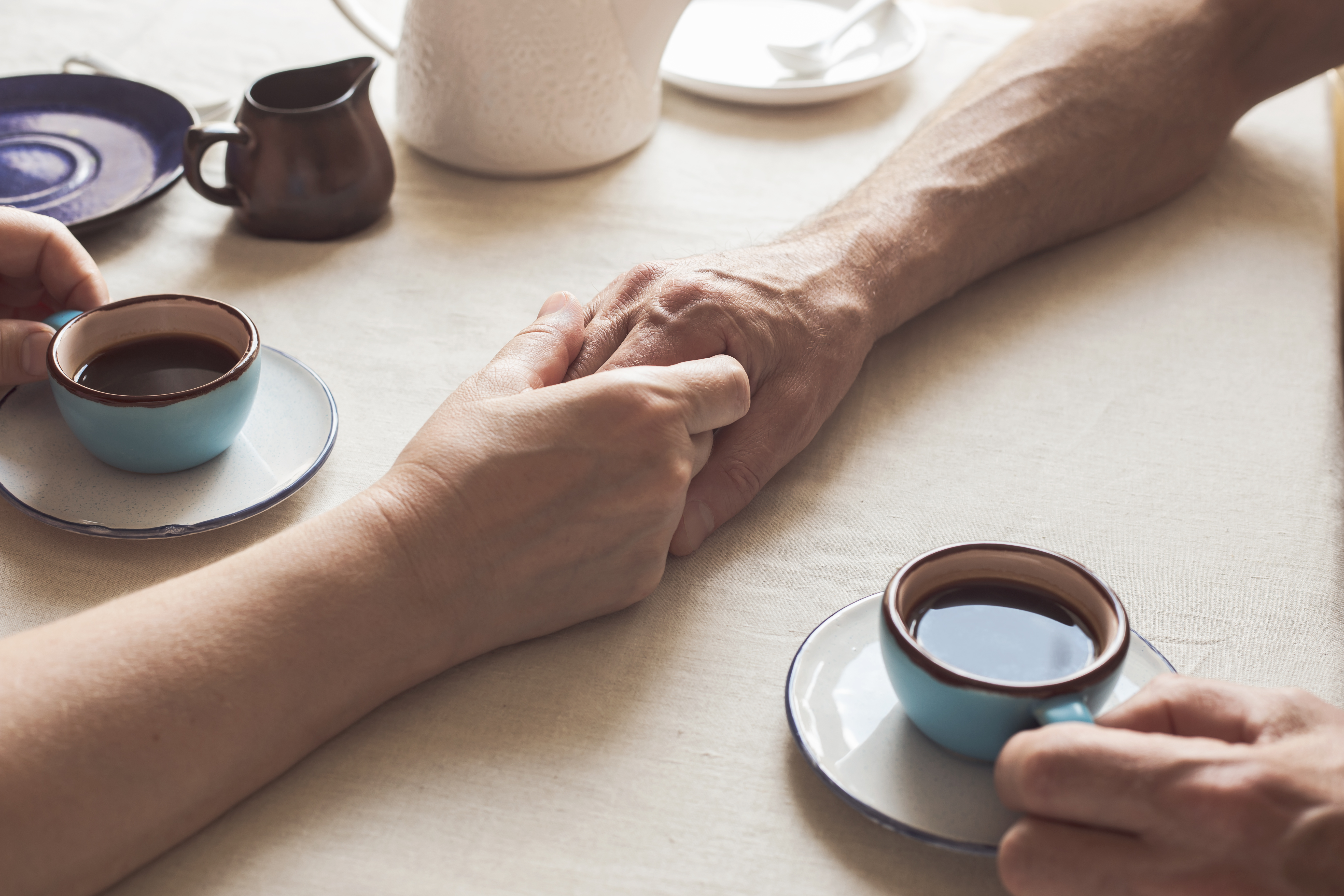 Cropped image of senior couple holding hands and drinking coffee | Source: Getty Images