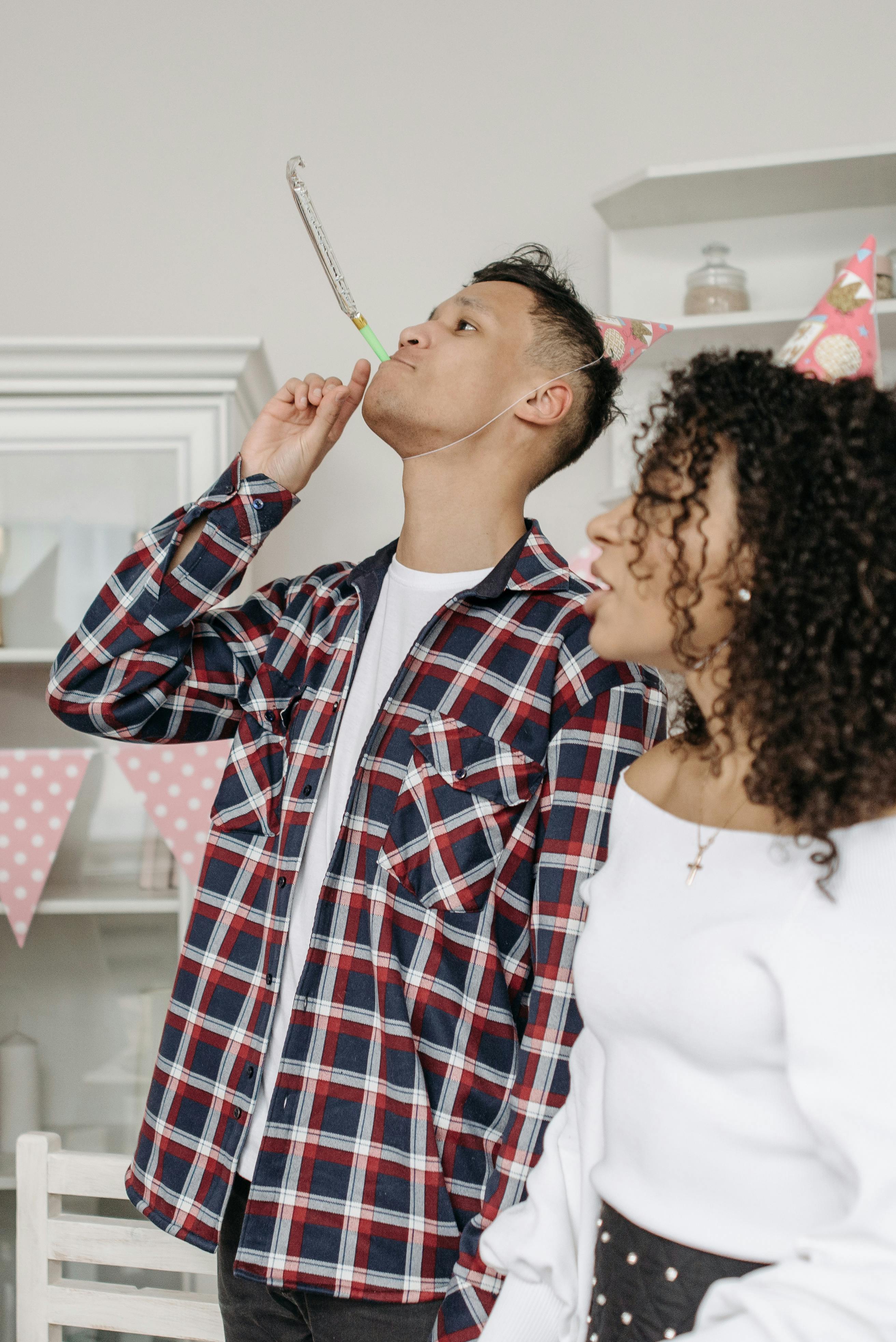 A man blowing a party horn during a birthday party while a woman stands next to him | Source: Pexels