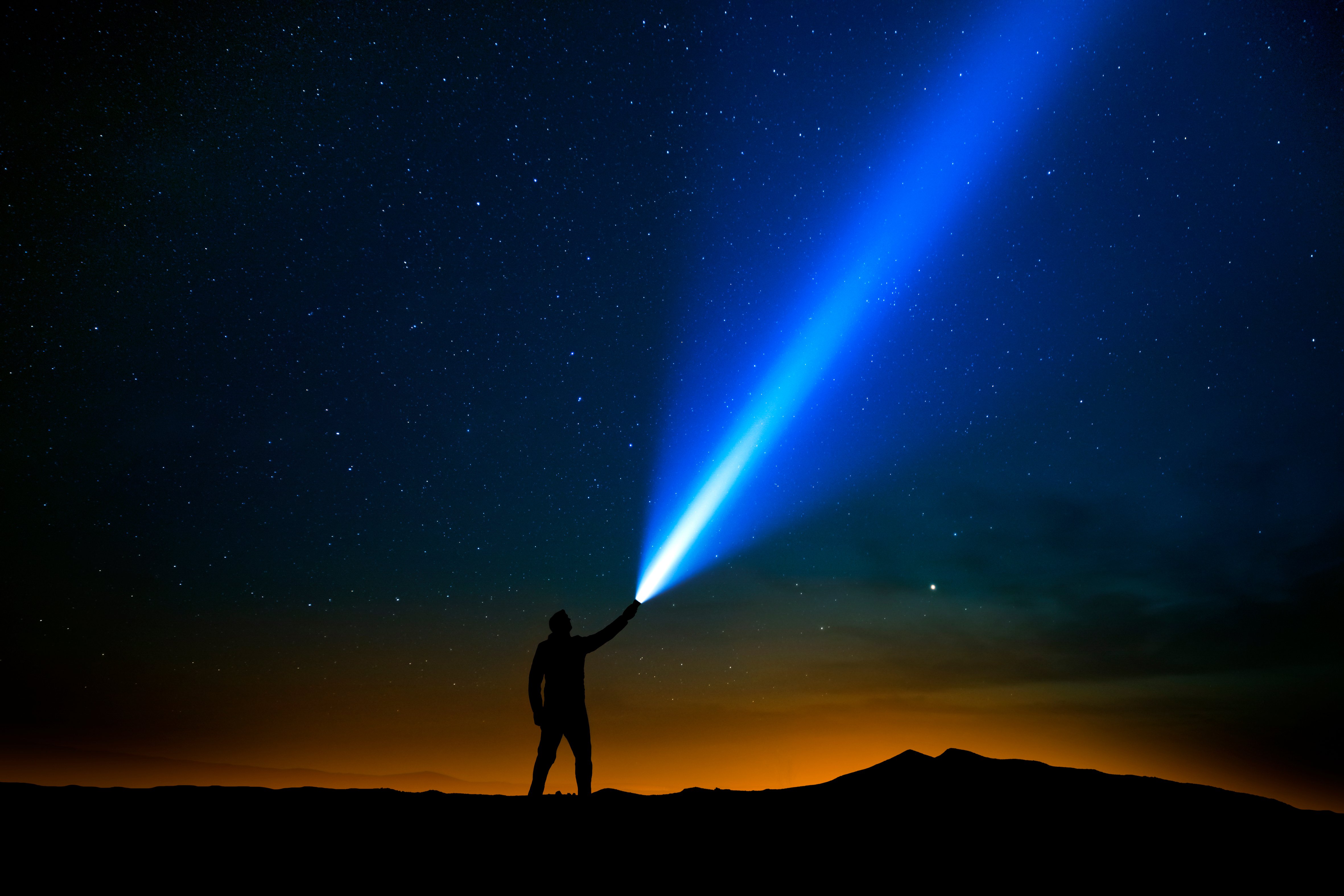 Hombre alumbrando con una linterna hacia el cielo de la noche. | Foto: Shutterstock