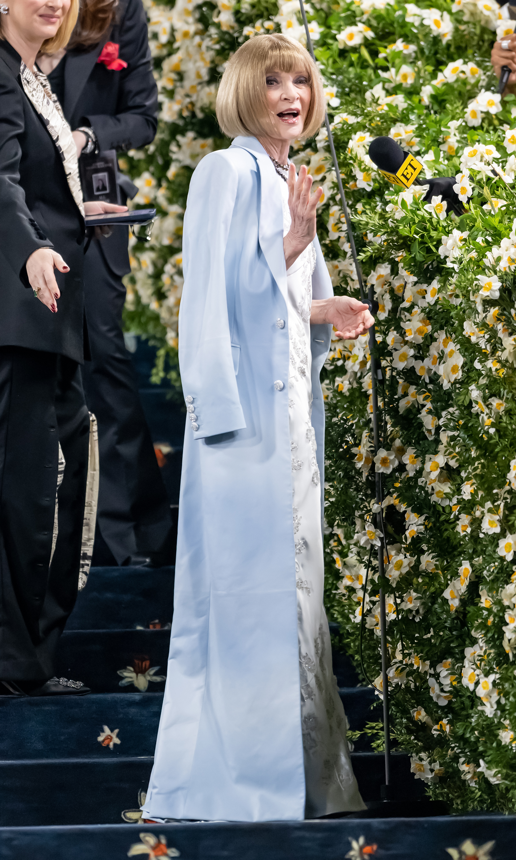 On the Met Gala steps, Anna Wintour speaks to media in her silk gown and pale blue coat. The 2025 event centered around "Superfine: Tailoring Black Style," celebrating Black designers and fashion's cultural legacy.