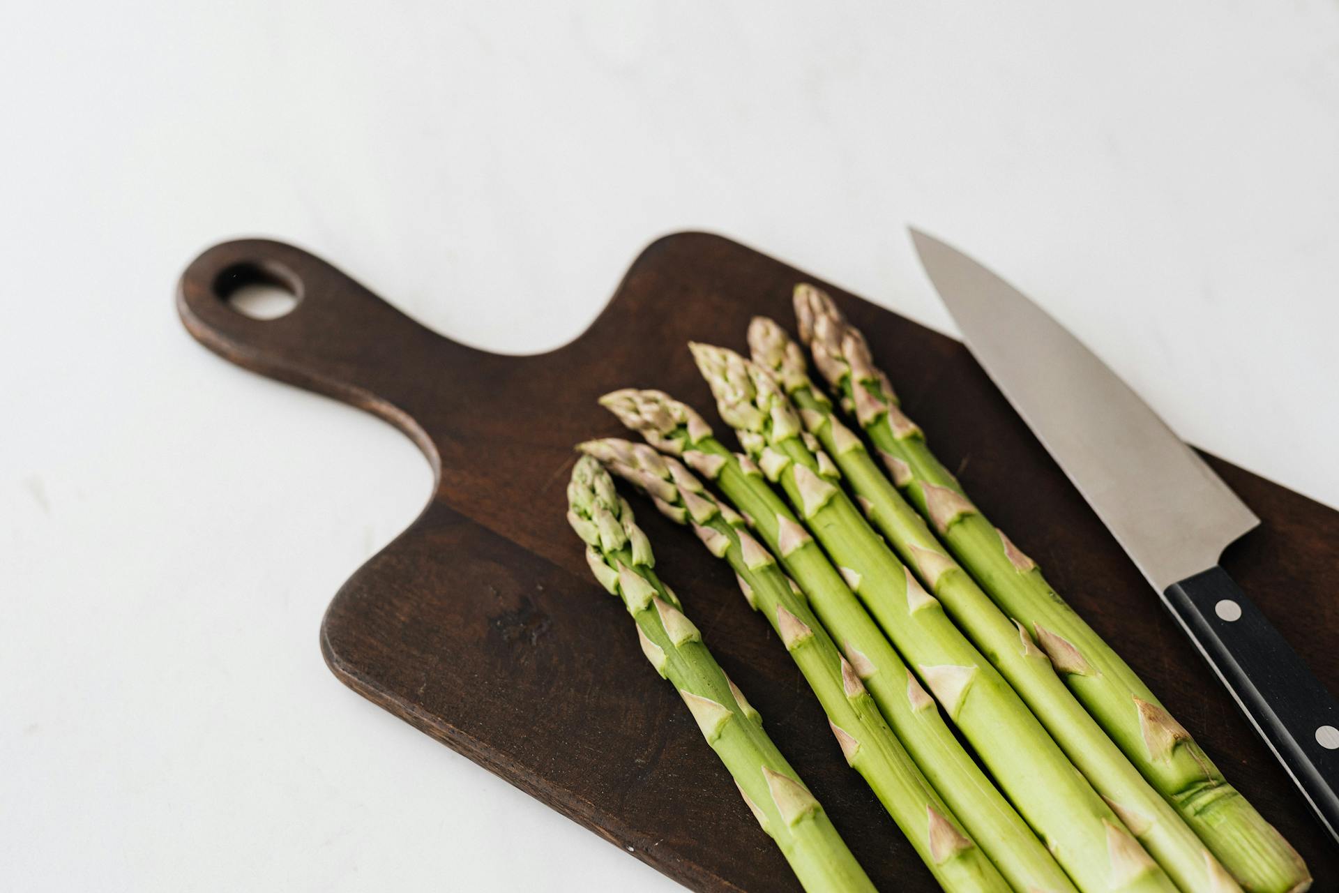 Fresh asparagus on a wooden board with a knife | Source: Pexels