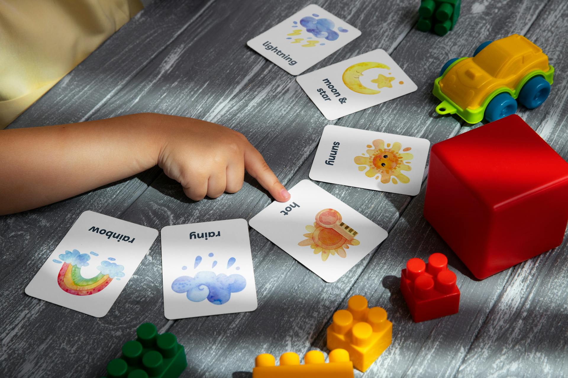 A close-up of a child pointing at a card lying on a table with blocks | Source: Pexels
