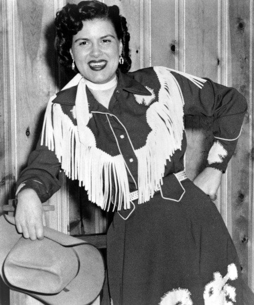 Patsy Cline plays the piano wearing a fringed dress and holding a cowboy hat in circa 1958. | Photo: Getty Images