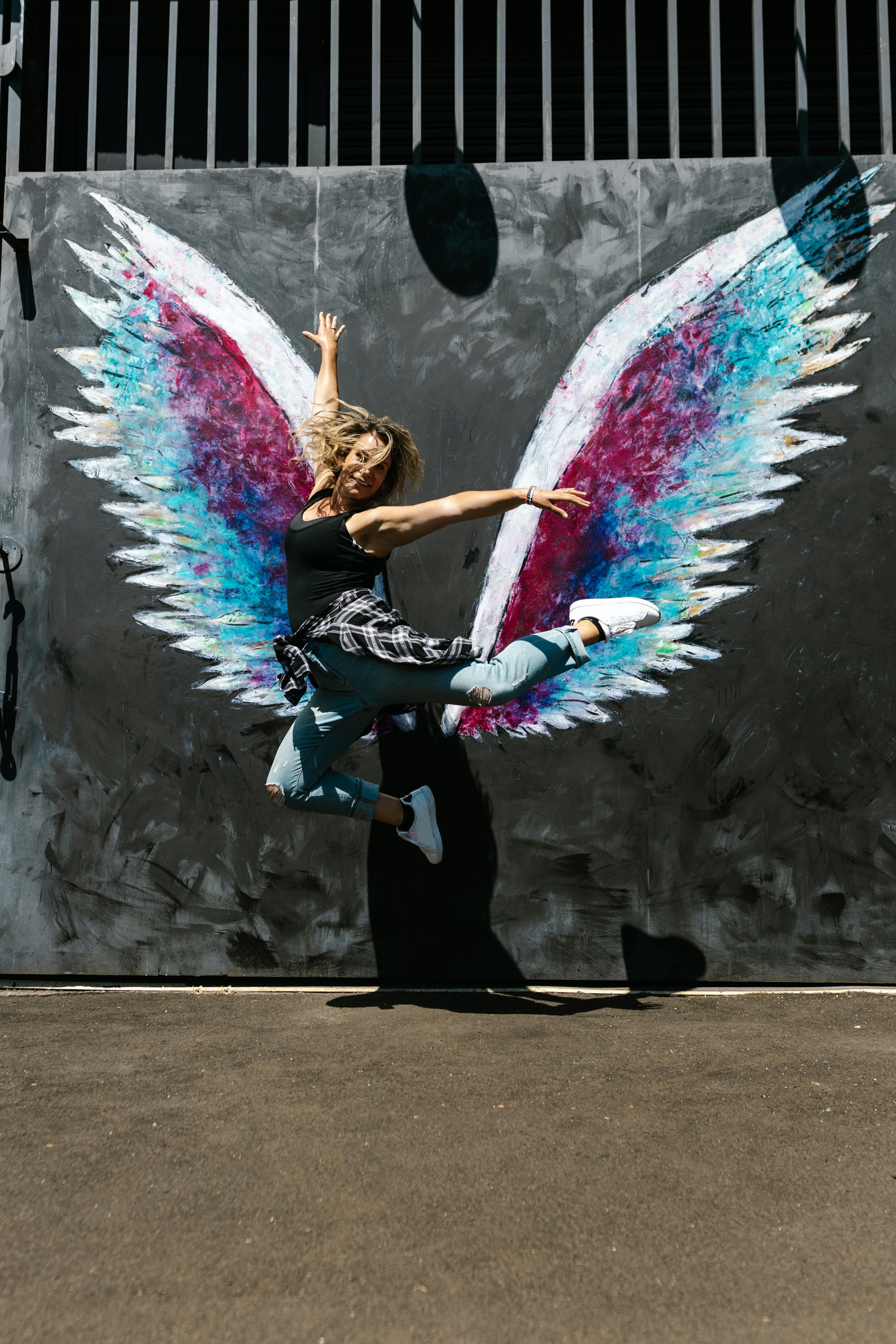 A woman jumping in front of a wall with painted wings. | Source: Pexels