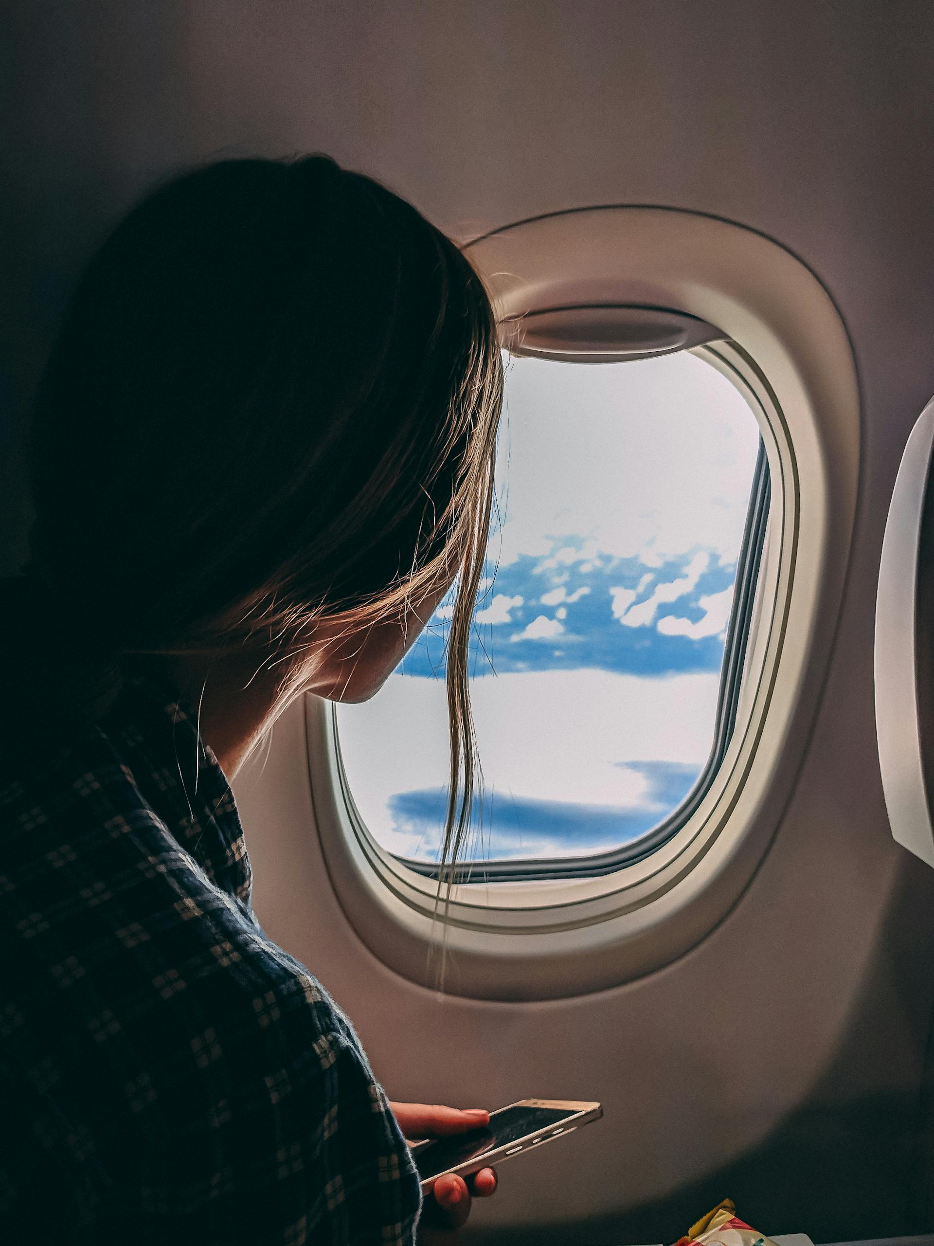 A woman holding her smartphone while riding in an airplane | Source: Pexels