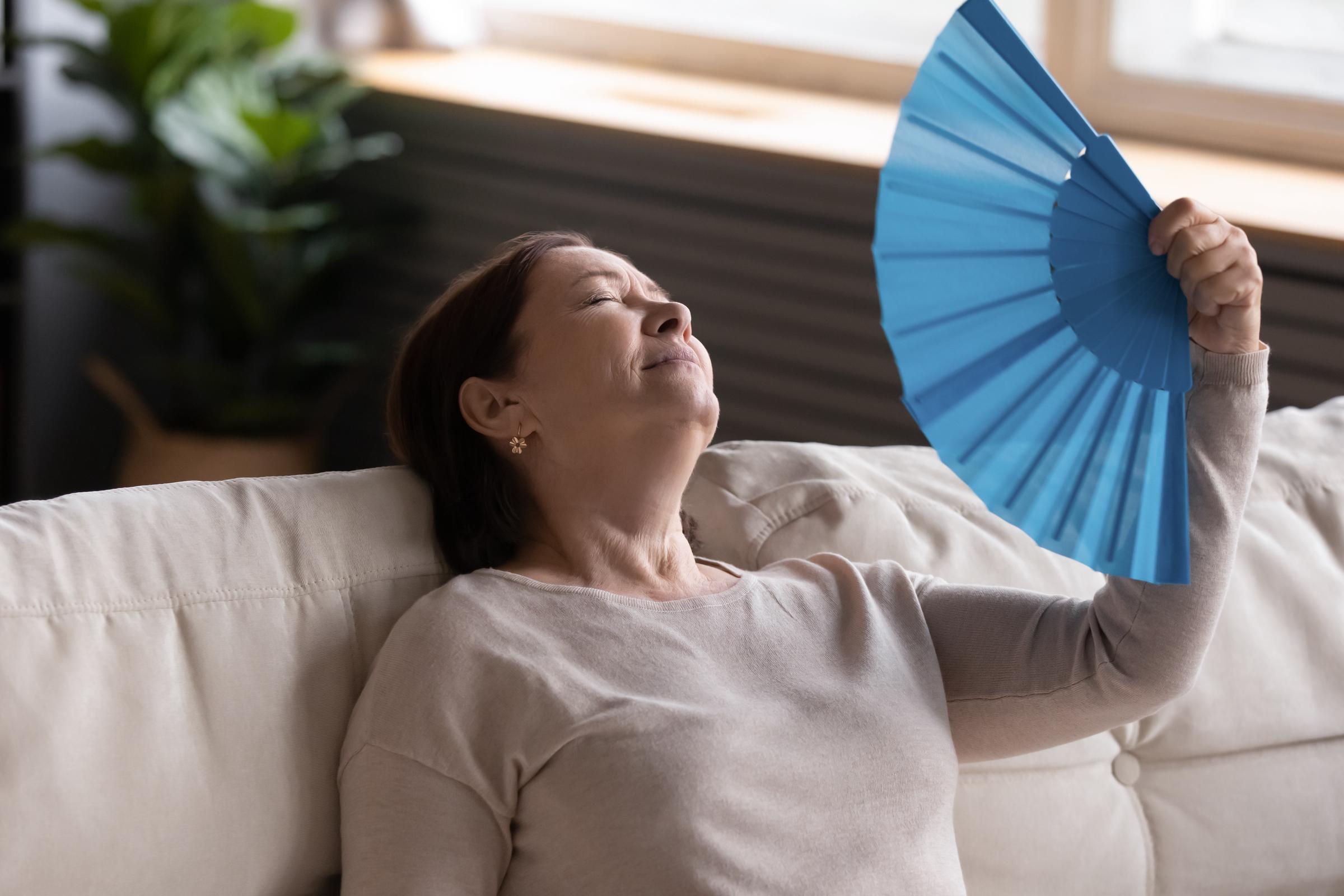 A woman fanning herself while lying on the couch | Source: Shutterstock