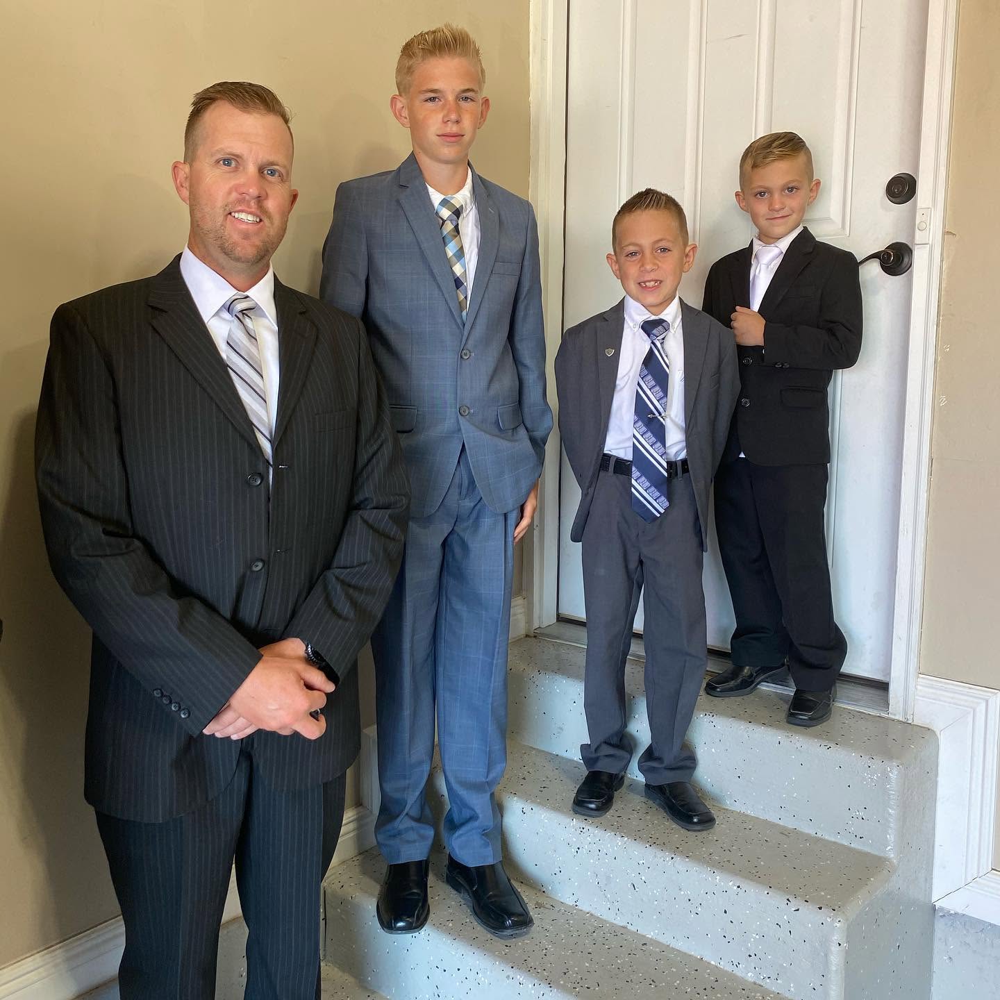 Spencer stands at the forefront with hands respectfully clasped, posing indoors with his three handsome sons, Reid, Thayne, and Gage, on a nearby stairway. The quartet looks unified and sharp in their tailored suits, representing a legacy of strength and unity. | Source: Facebook/katrina.g.long