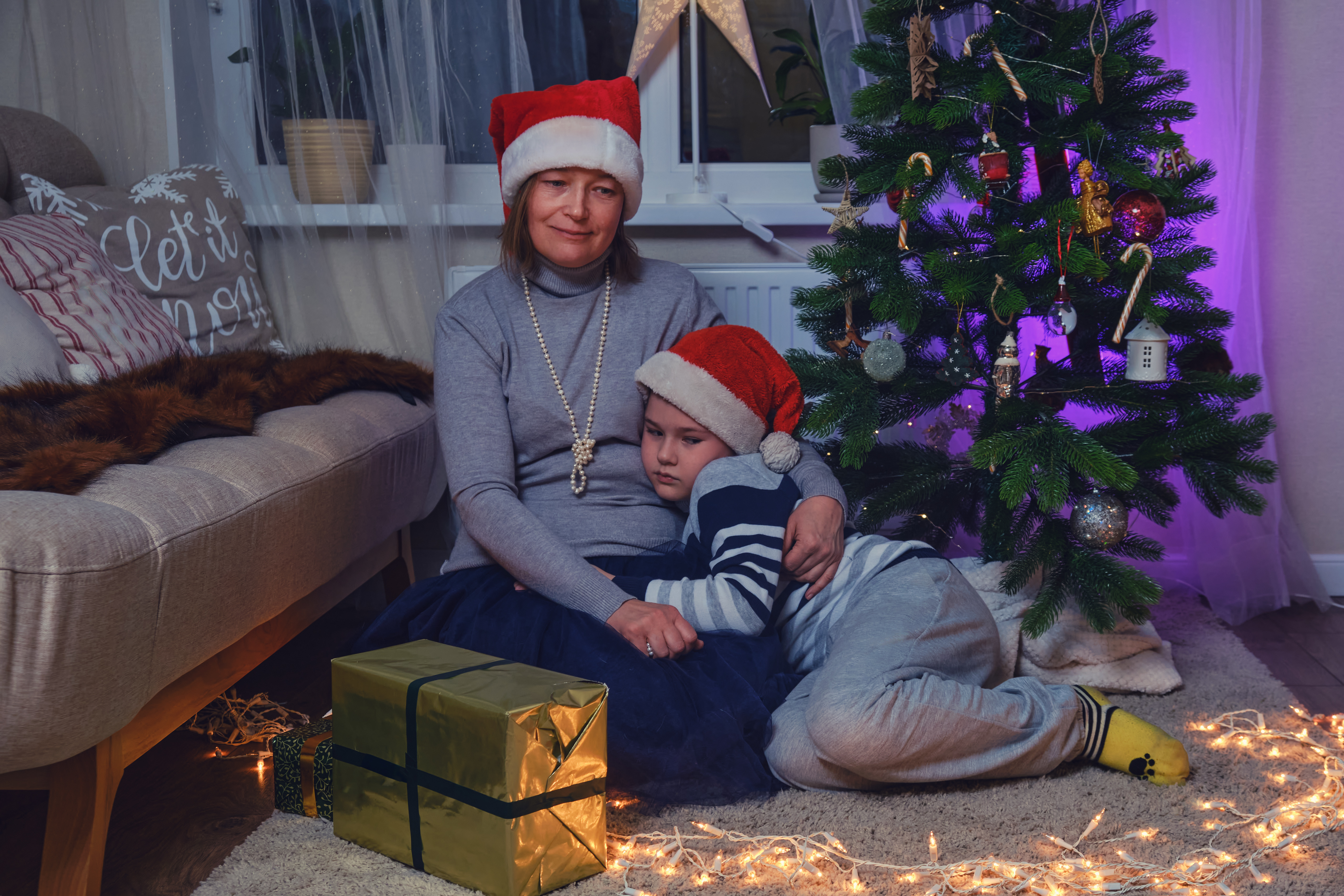 Sad mother and son sitting near the Christmas tree in the night light garlands. | Source: Getty Images