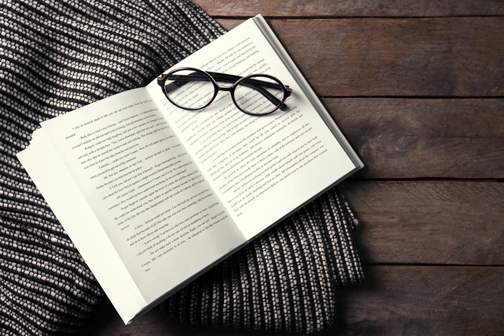 Un libro abierto, gafas y una manta sobre el fondo de madera. | Foto: Shutterstock.