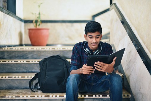 Teenager student using digital tablet while sitting on stairway | Photo: Getty Images