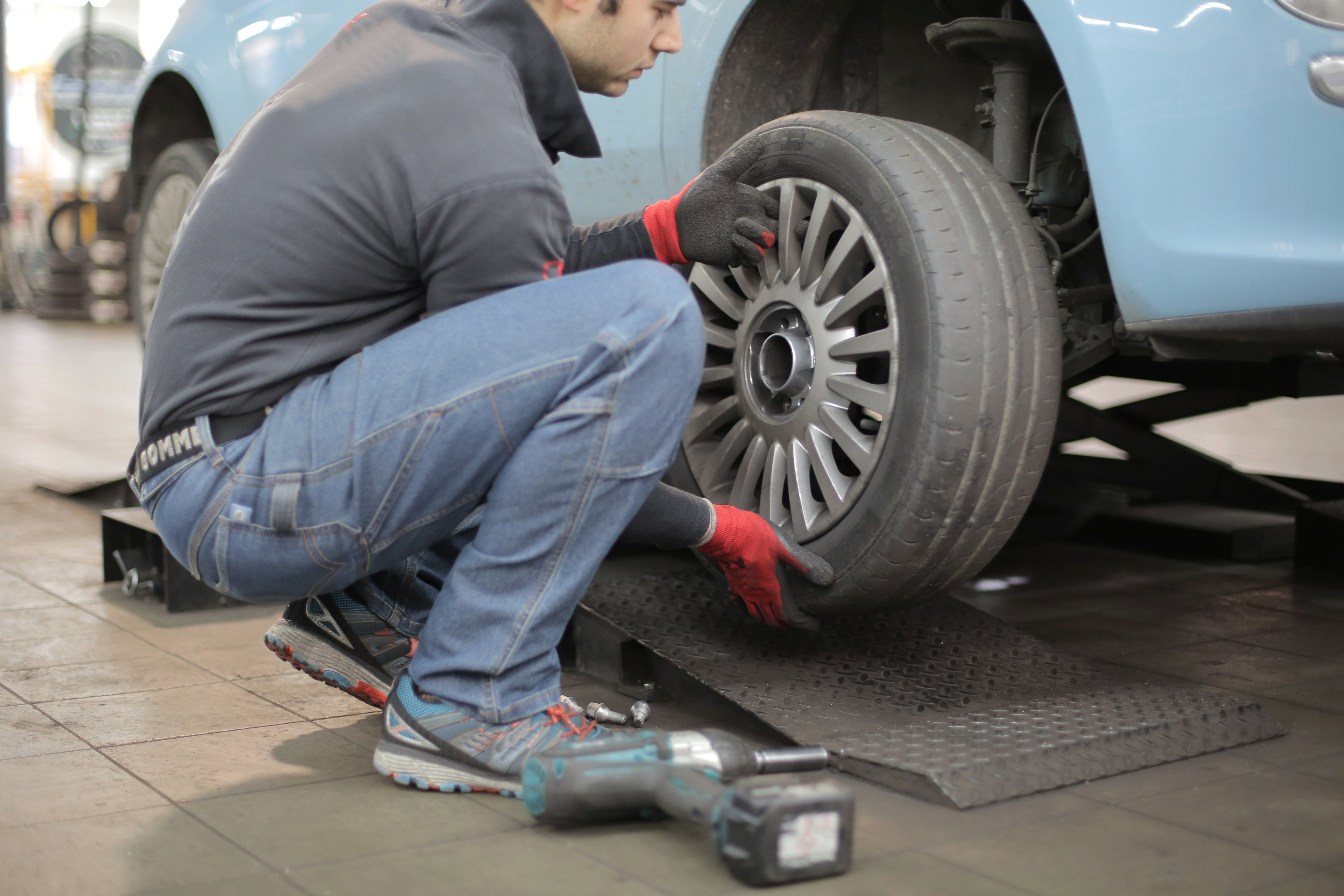 Pictured - A photo of a man changing a tire wearing jeans, a gray jacket and matching gloves | Source: Pexels 