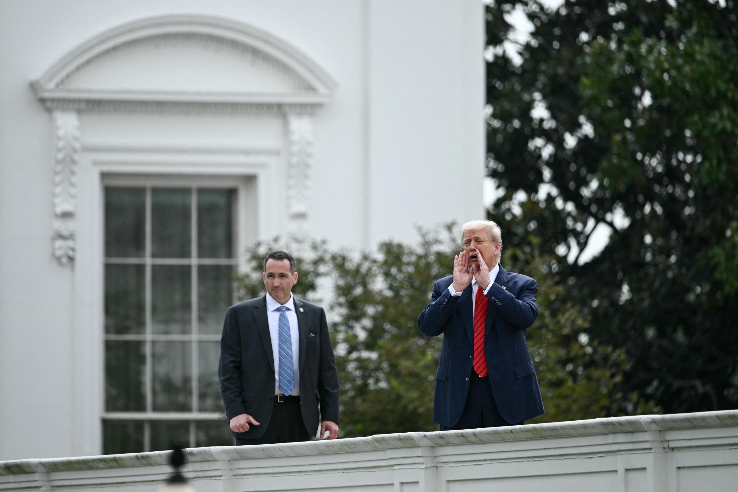 With his security team nearby, President Donald Trump calls out to the press from the West Wing roof of the White House in Washington, D.C., on August 5.