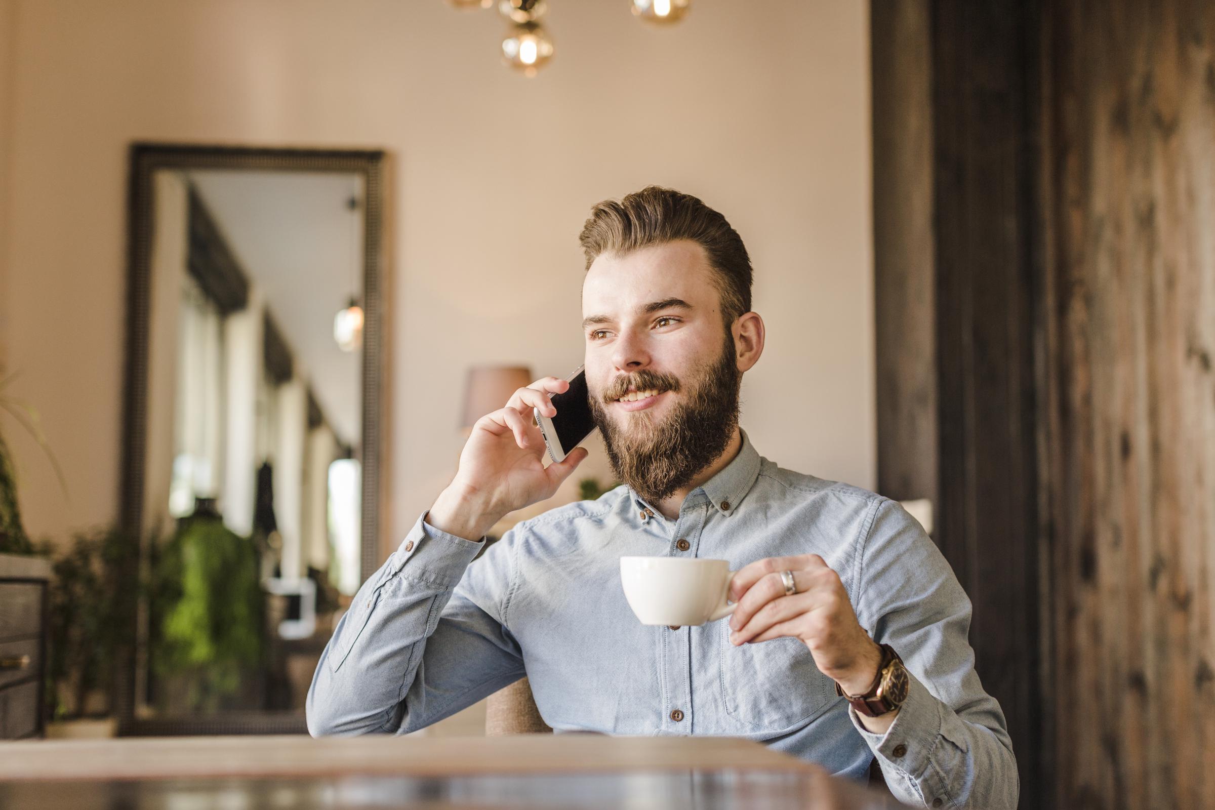 A smiling man on the phone talking while drinking coffee | Source: Freepik