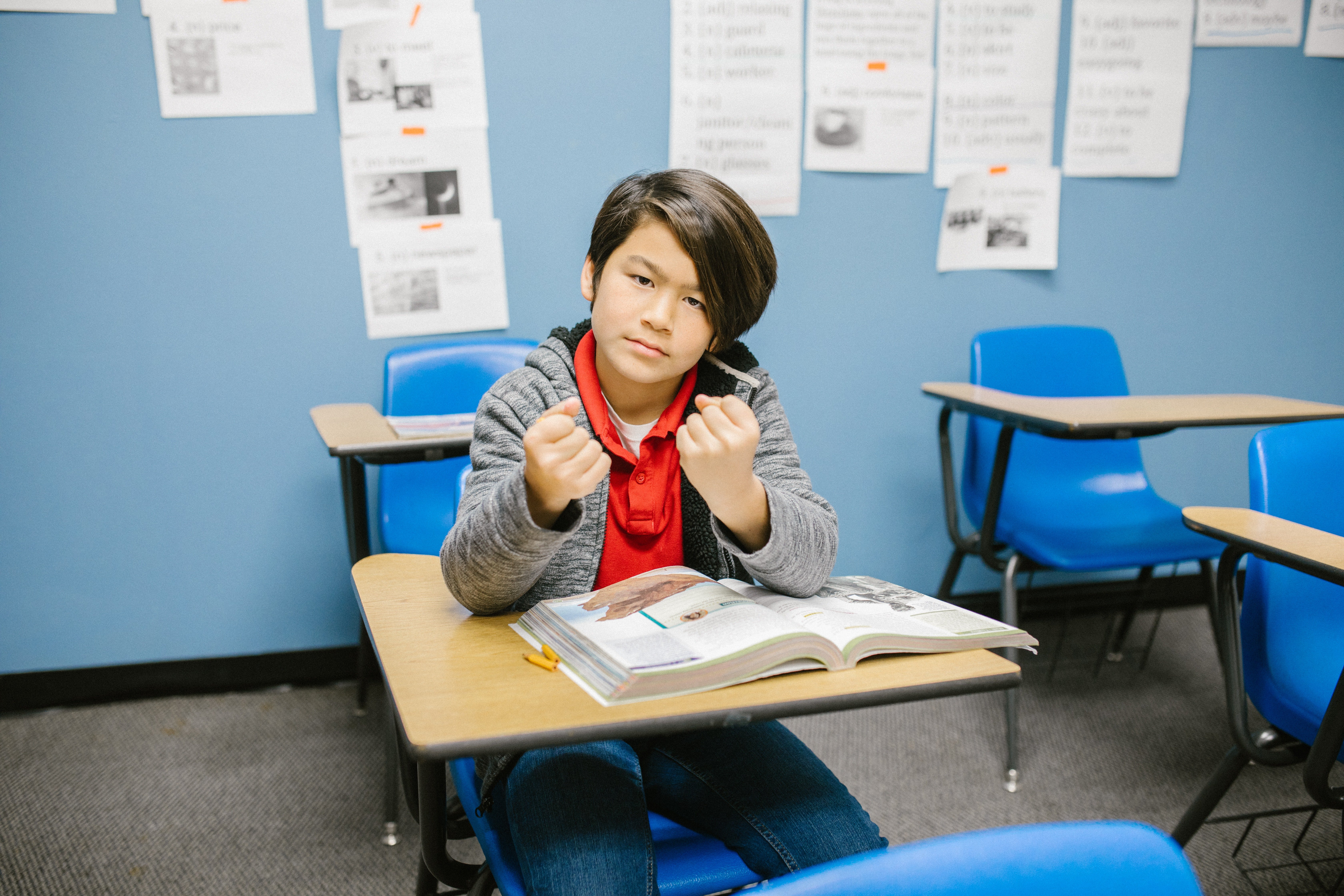 Niño sentado en un salón de clases mostrando sus puños. | Foto: Pexels