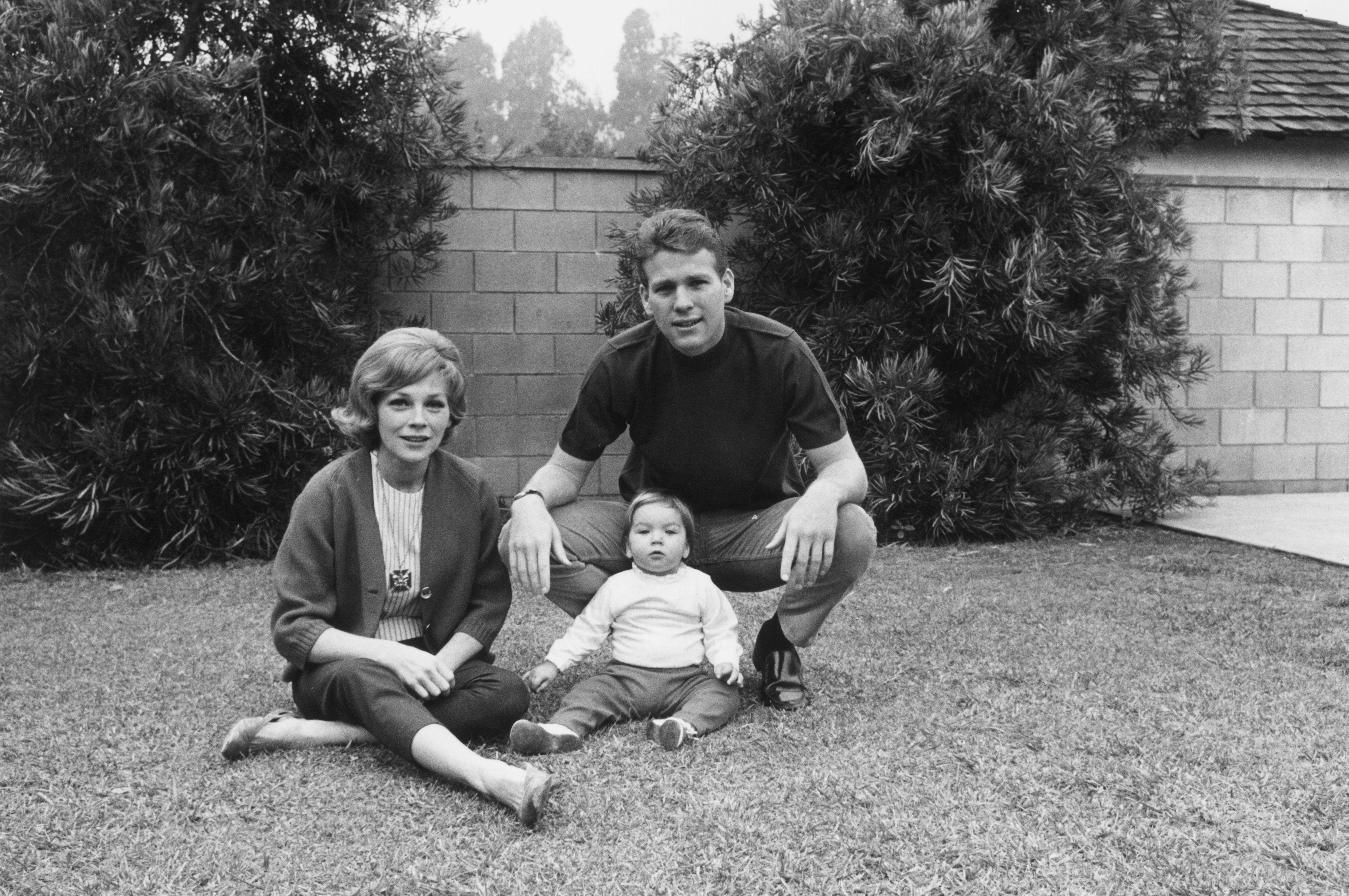 Ryan O'Neal with his wife, actor Joanna Moore, and daughter, Tatum, sitting on grass in front of a stone wall | Photo: Getty Images