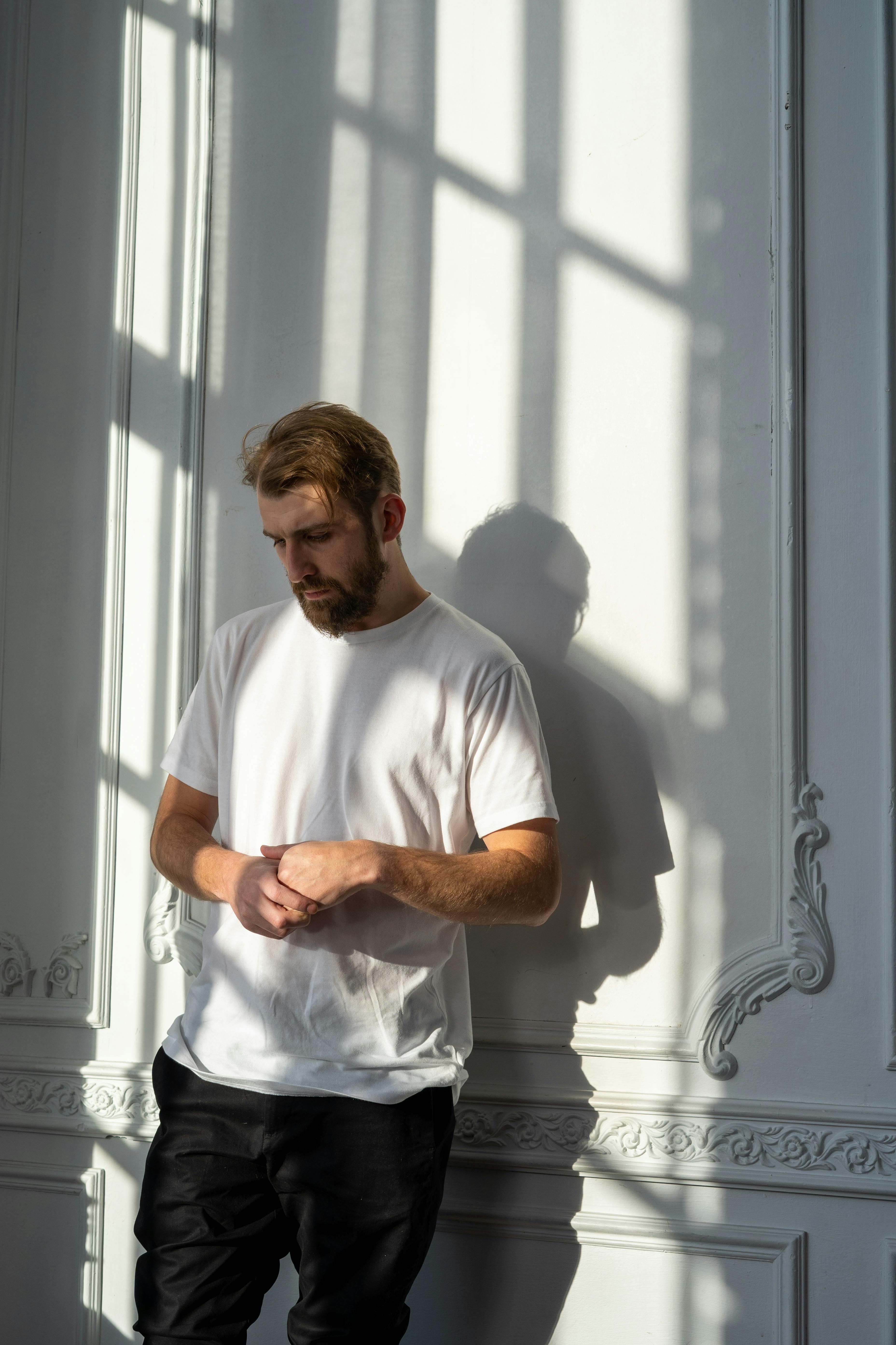 A sad-looking man standing against a wall looking down | Source: Pexels