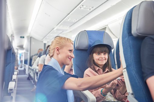 Flight attendant helping girl passenger on airplane | Photo: Getty Images