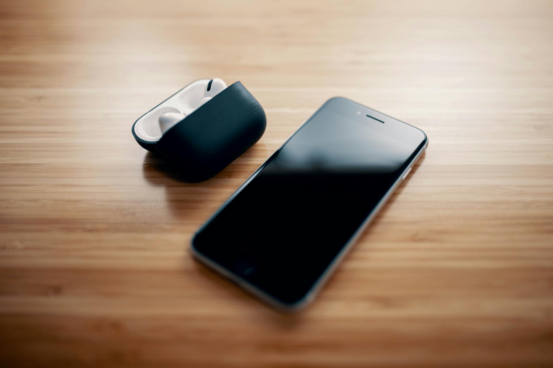 A black smartphone and earbuds lying on a table | Source: Pexels