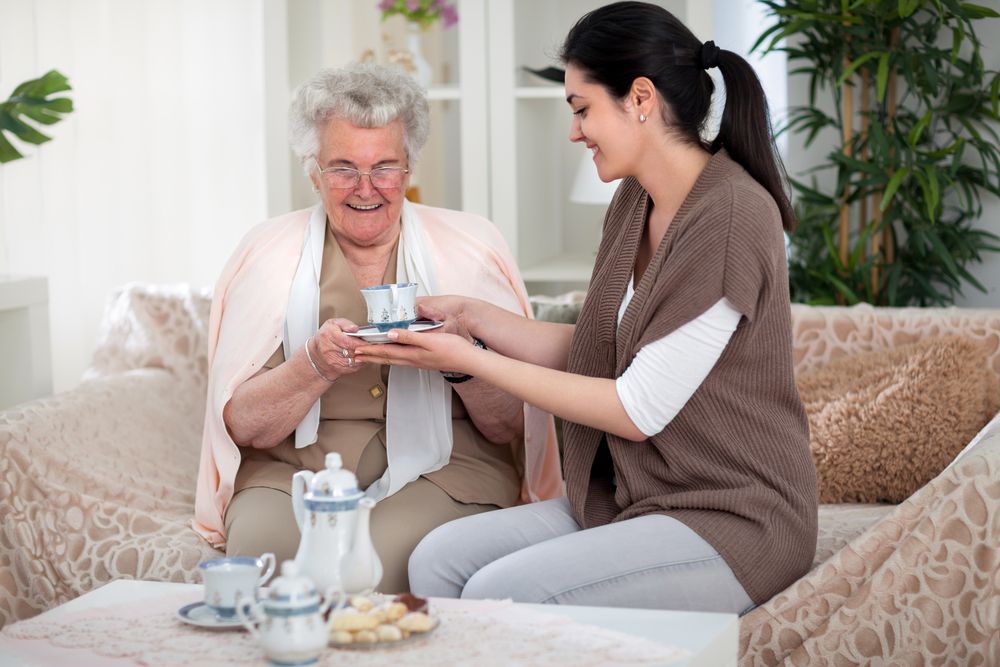 A woman giving an elderly lady a cup of tea. │Source: Shutterstock