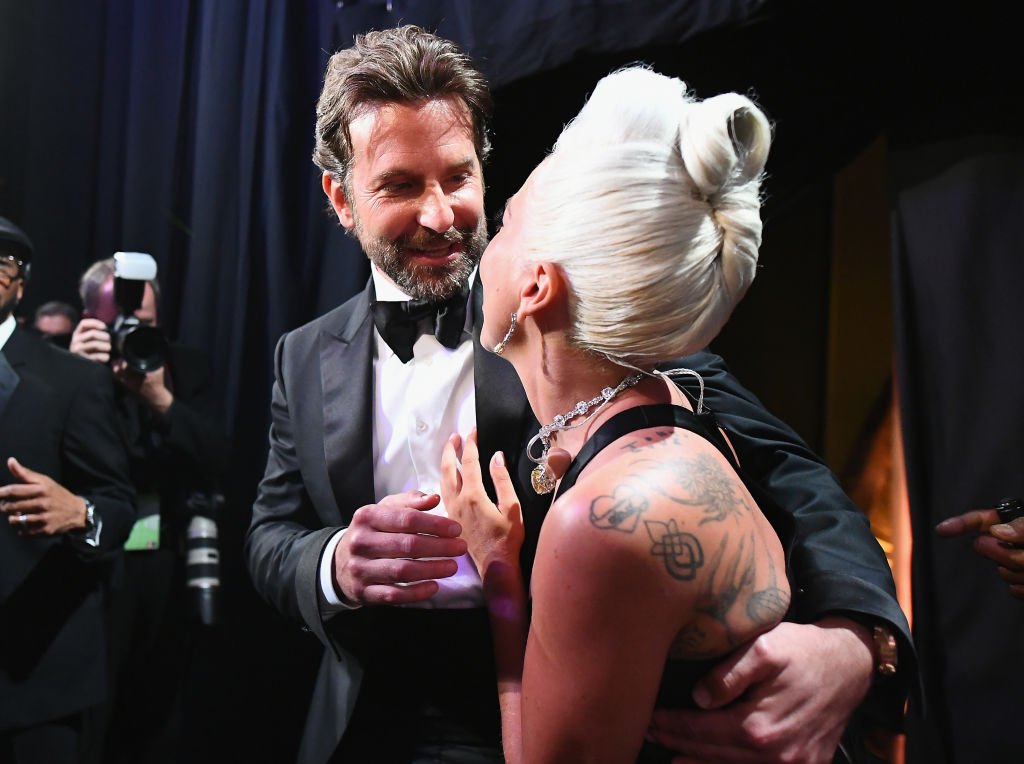 Bradley Cooper toma por la espalda a Lady Gaga mientras ambos lucen muy sonrientes. | Foto: Getty Images