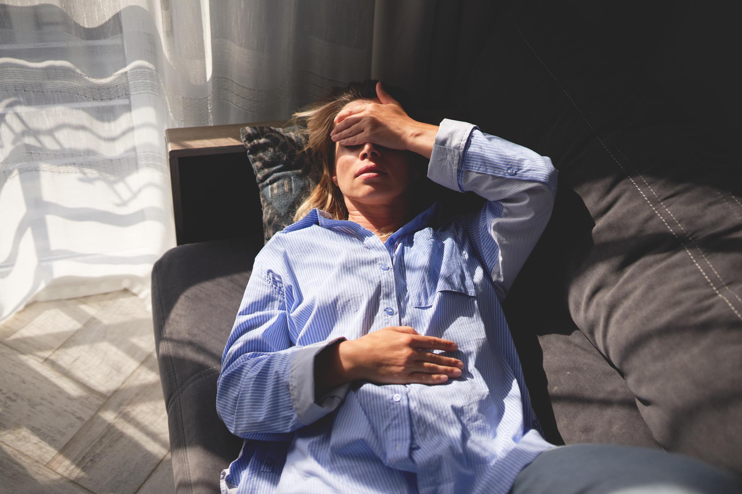 Woman lying on a couch with her hand on her forehead and eyes closed, indicating exhaustion or stress | Source: Getty Images