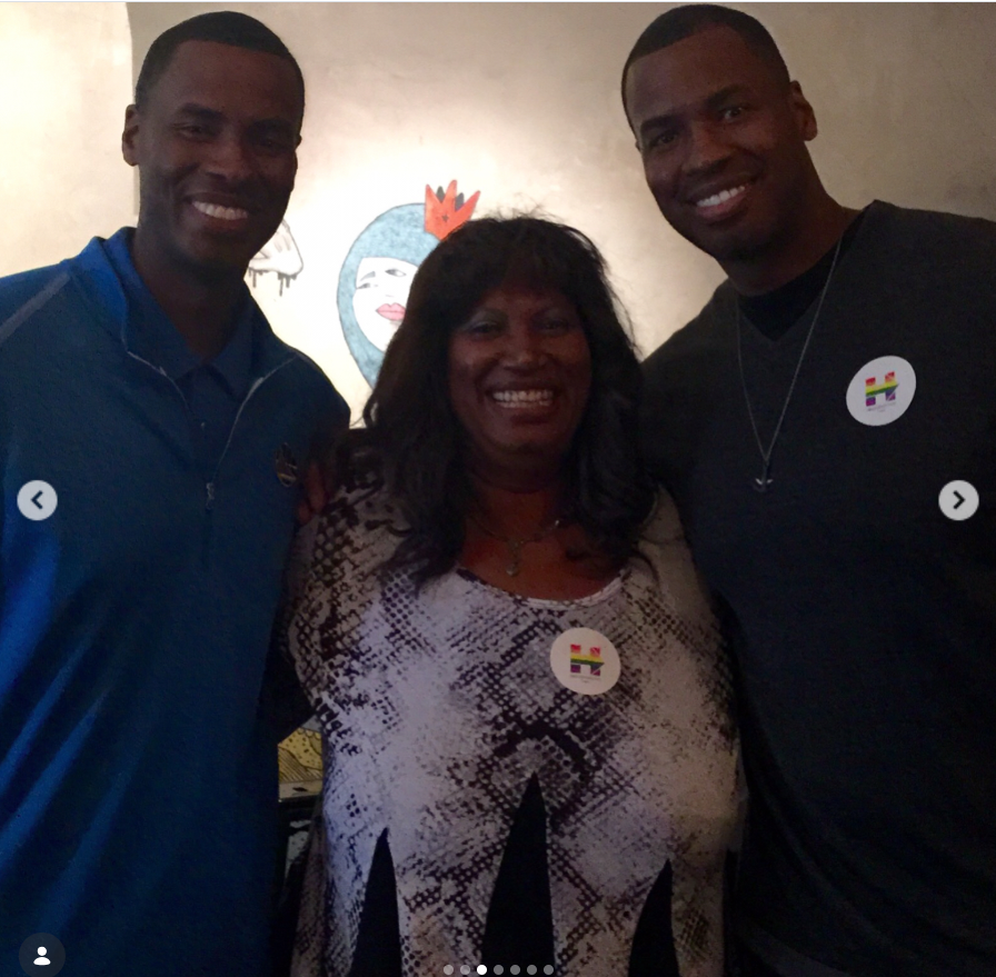 Jason Collins and his twin brother, Jarron Collins, pose beside their mother, Portia Collins, during a gathering while wearing matching rainbow-themed pins in support of LGBTQ+ pride. | Source: Instagram/jasoncollins_98