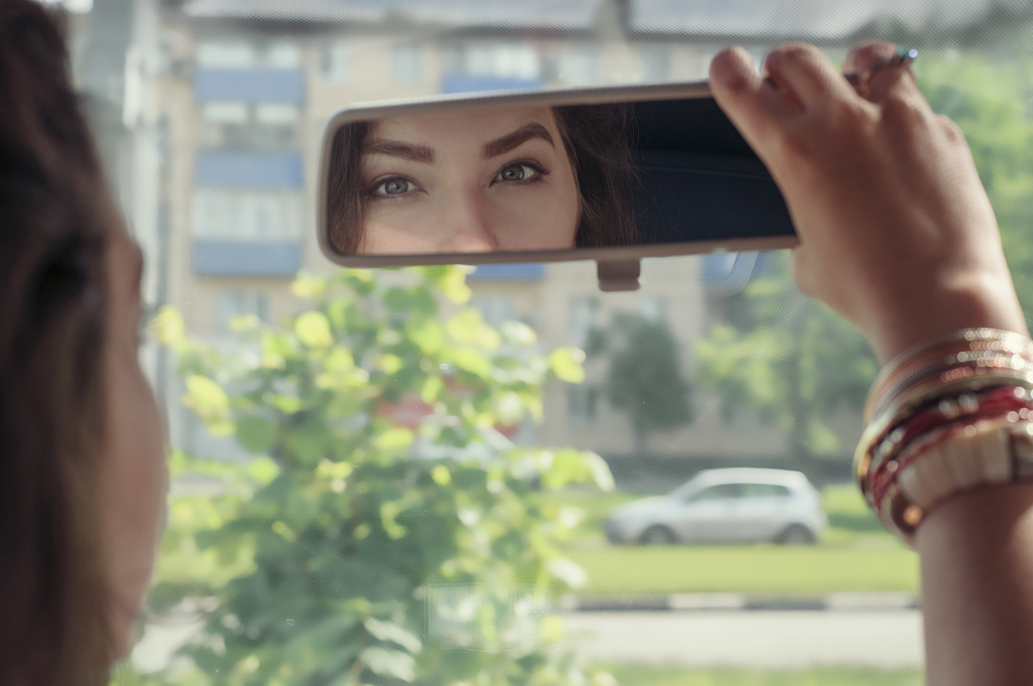 Woman looking at her reflection in the rearview mirror of car | Source: Shutterstock.com