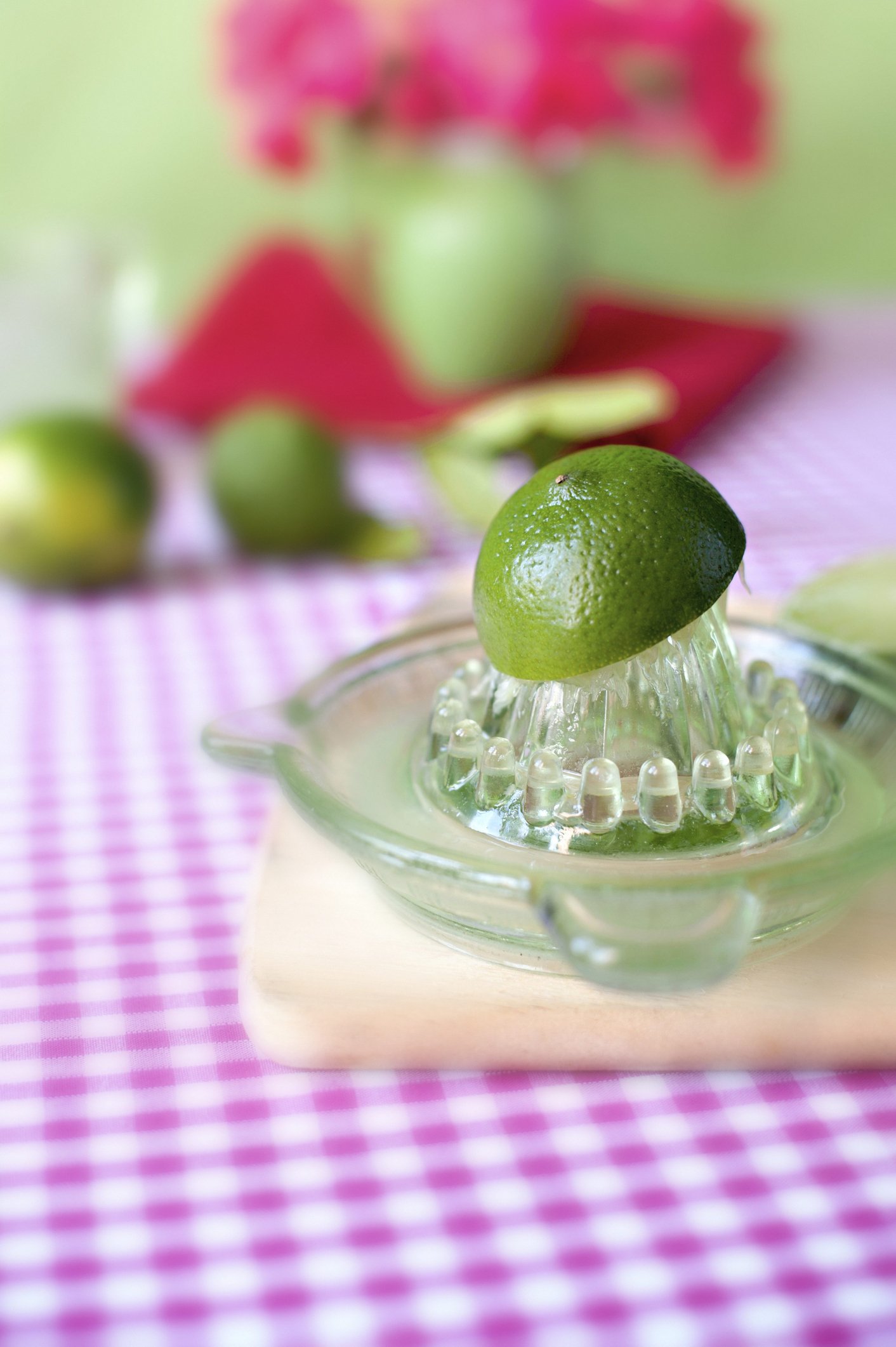 Fresh limes on a red and white gingham cloth being hand juiced in a vintage green glass juicer. | Photo: Getty Images