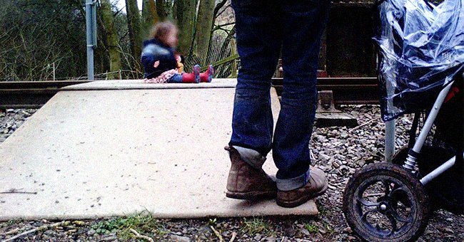 A parent looking on as their toddler sits on a railway crossing. │Source: twitter.com/WalesOnline